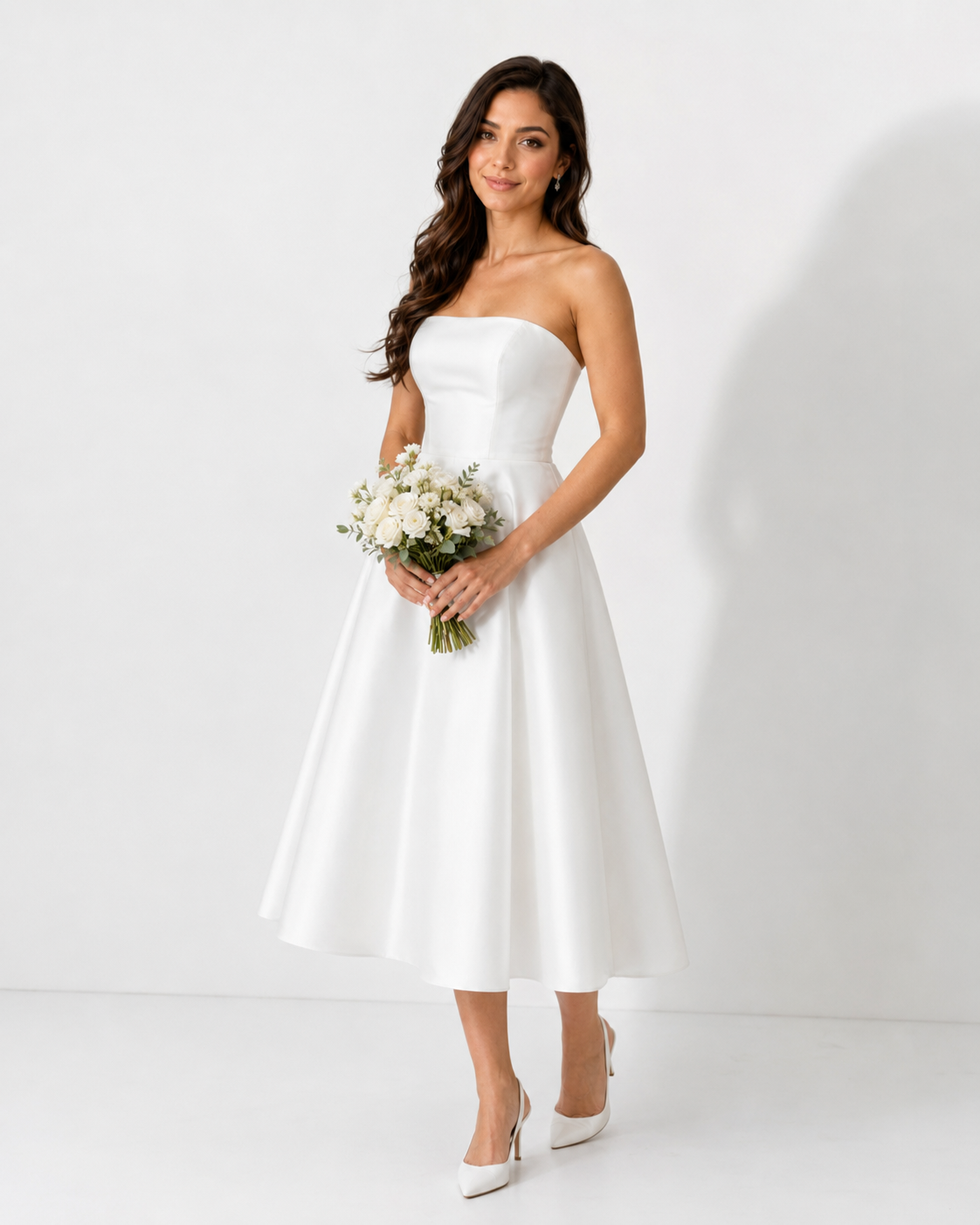 Woman wearing a strapless white midi wedding dress with full skirt, holding a white floral bouquet.