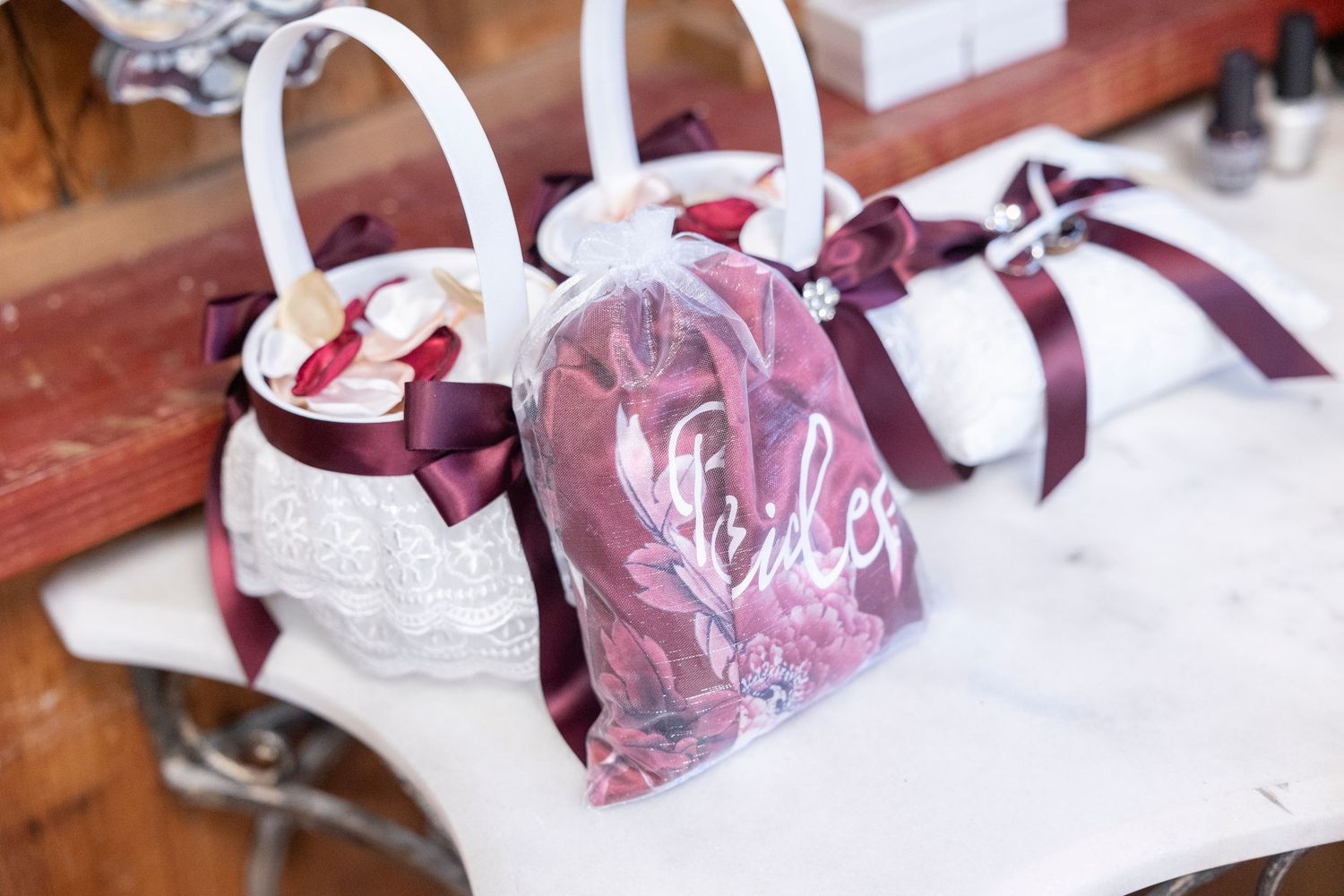 White lace flower girl baskets decorated with burgundy ribbons displayed on a table.