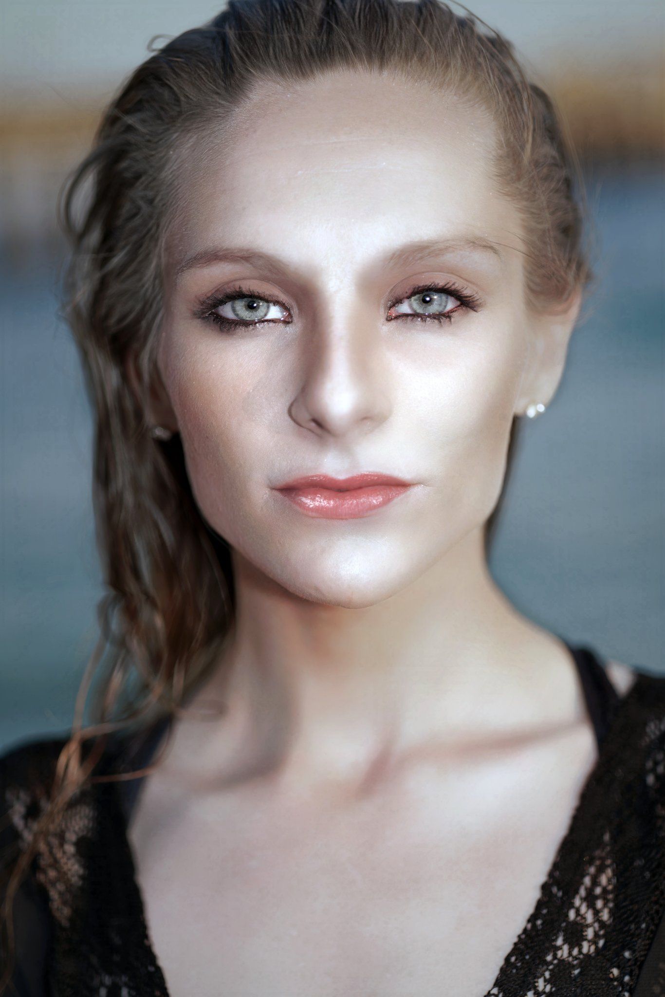 Close-up portrait of a young woman with green eyes, subtle makeup, pearl earring, and wet hair in a black lace top.