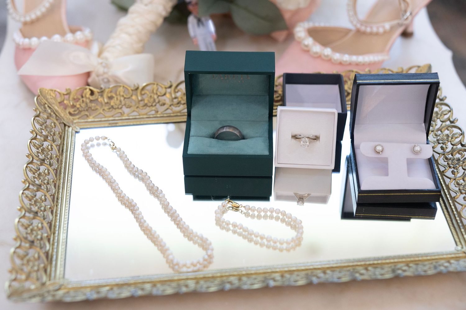 Elegant pearl necklace, bracelets, and rings displayed in jewelry boxes on a ornate gold mirrored tray.