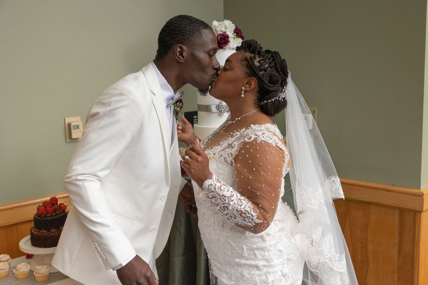 A bride and groom share a romantic kiss at their wedding ceremony, dressed in elegant white attire.