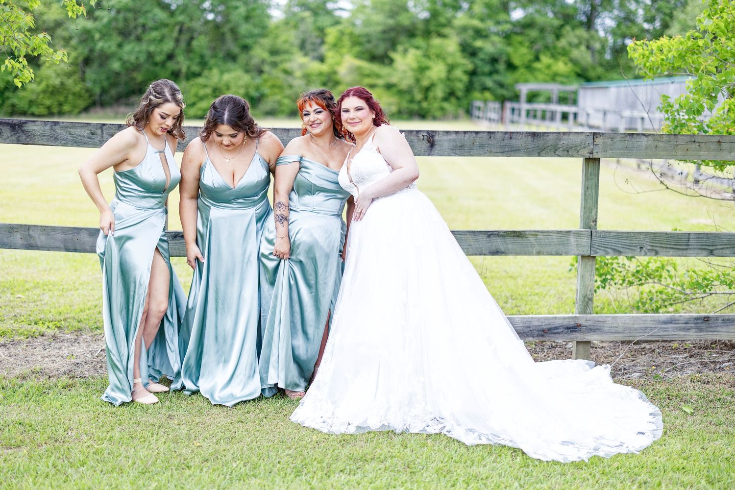 A group in light blue dresses poses together on grass near a wooden fence on a sunny day.