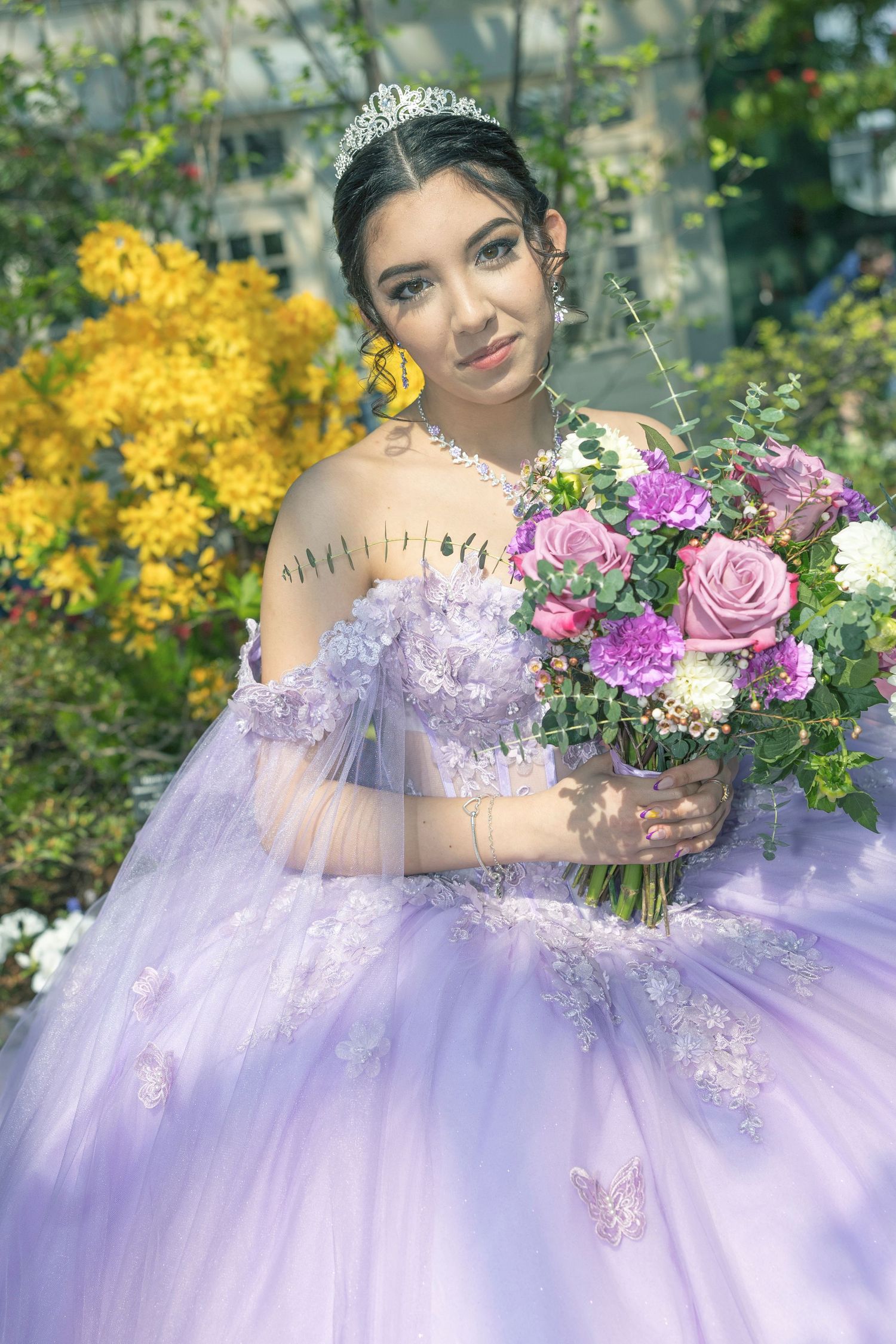 A dreamy quinceañera portrait featuring a lavender ballgown, sparkling tiara, and colorful bouquet against a garden backdrop.