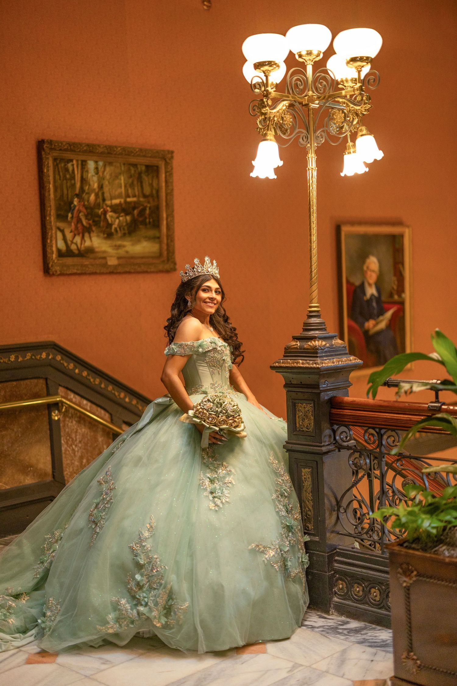 A mint green quinceañera ball gown with floral details is showcased in an elegant room with vintage furniture and decor.