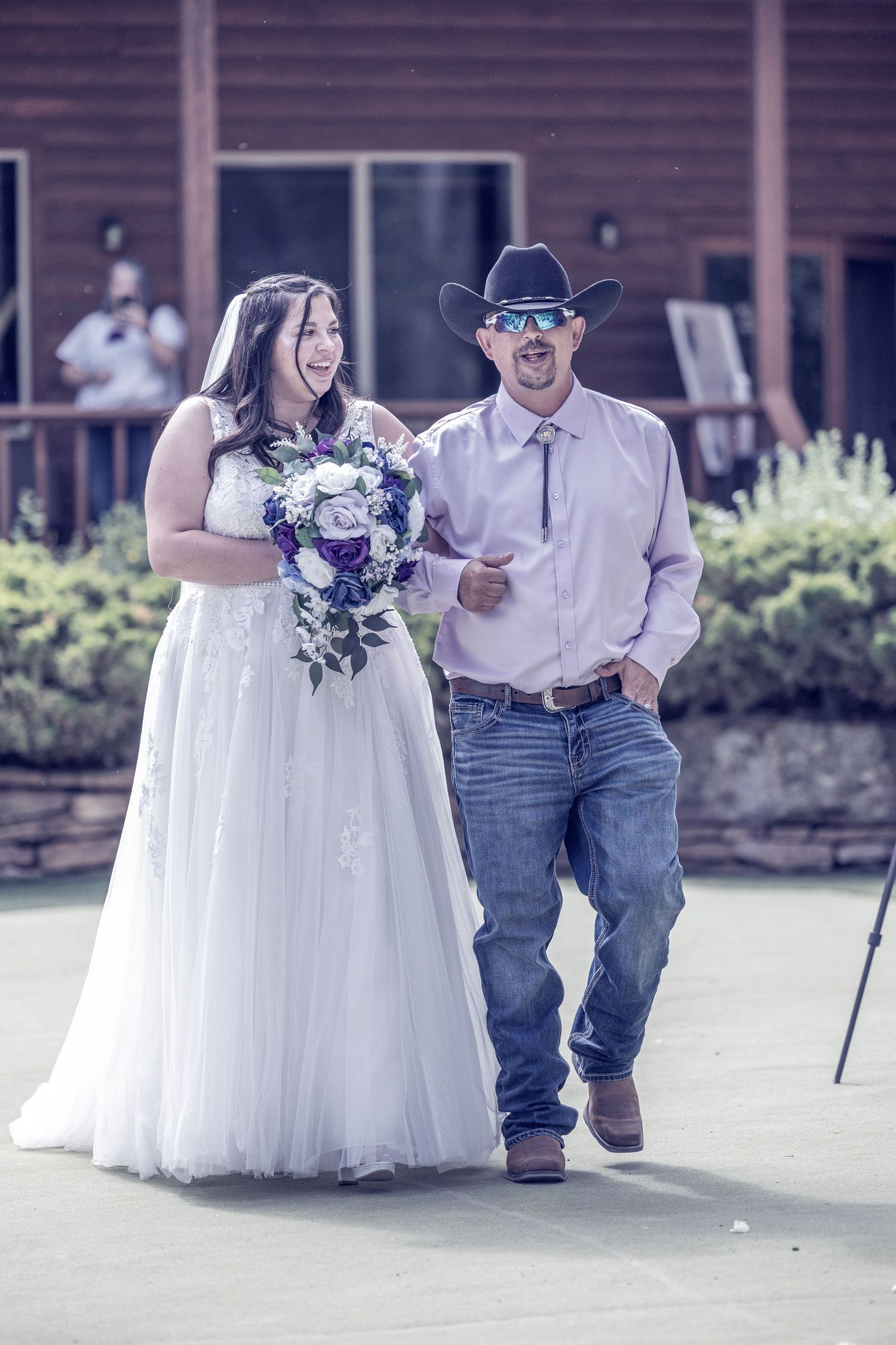 A bride in a white wedding dress and groom in cowboy hat share a joyful moment during their country-themed wedding ceremony.