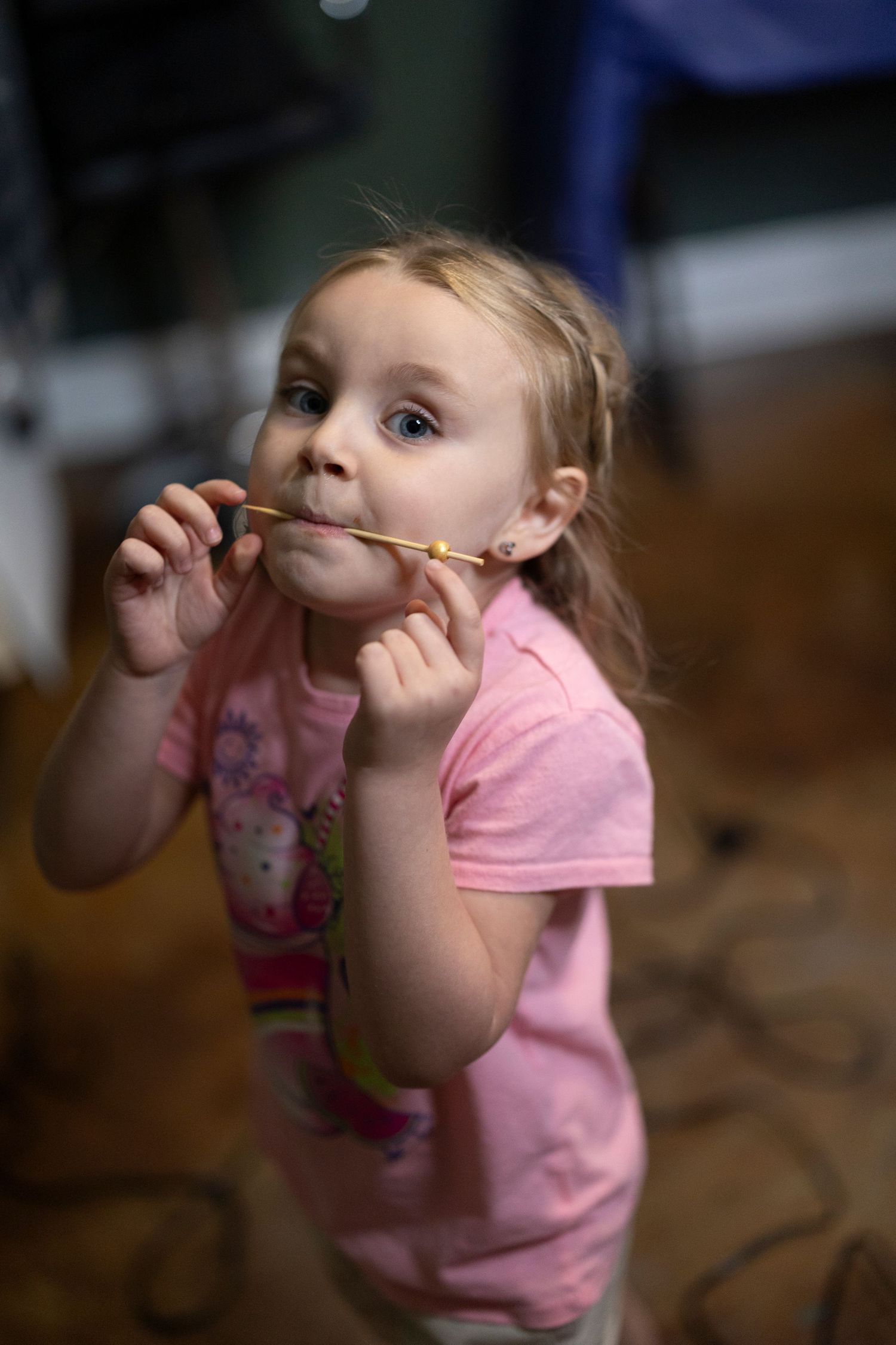 Young child in pink shirt playfully holds a pencil between their nose and upper lip.