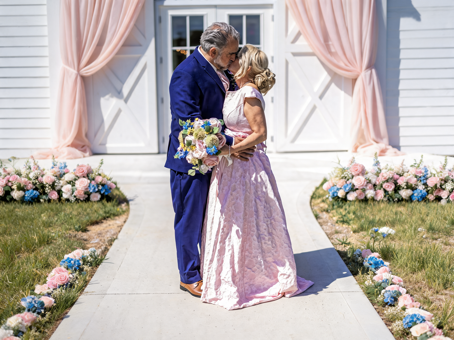 Couple sharing first kiss in pink wedding attire along floral-lined aisle outdoors.