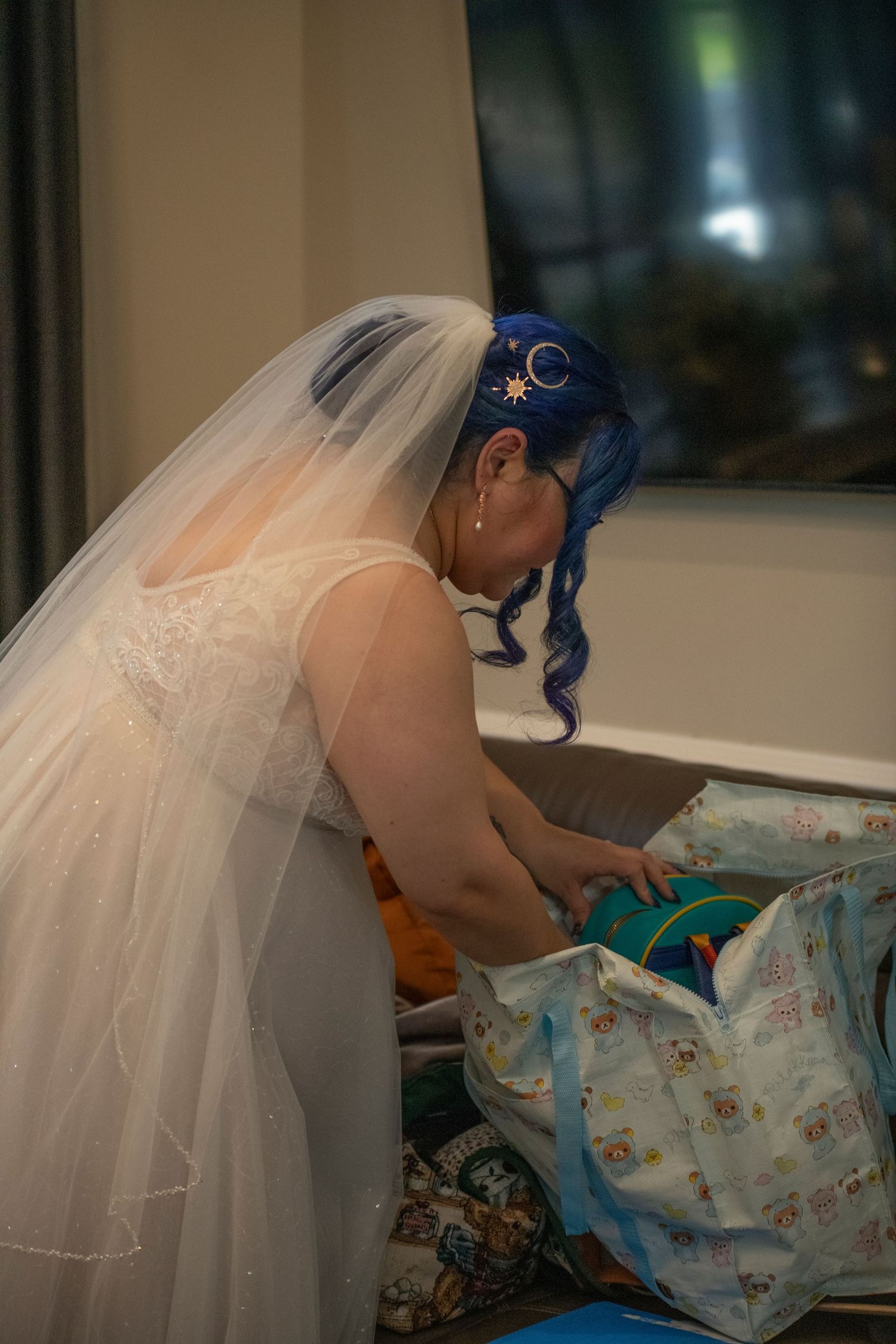 A bride in a white veil and blue hair leans over while getting ready on her wedding day.