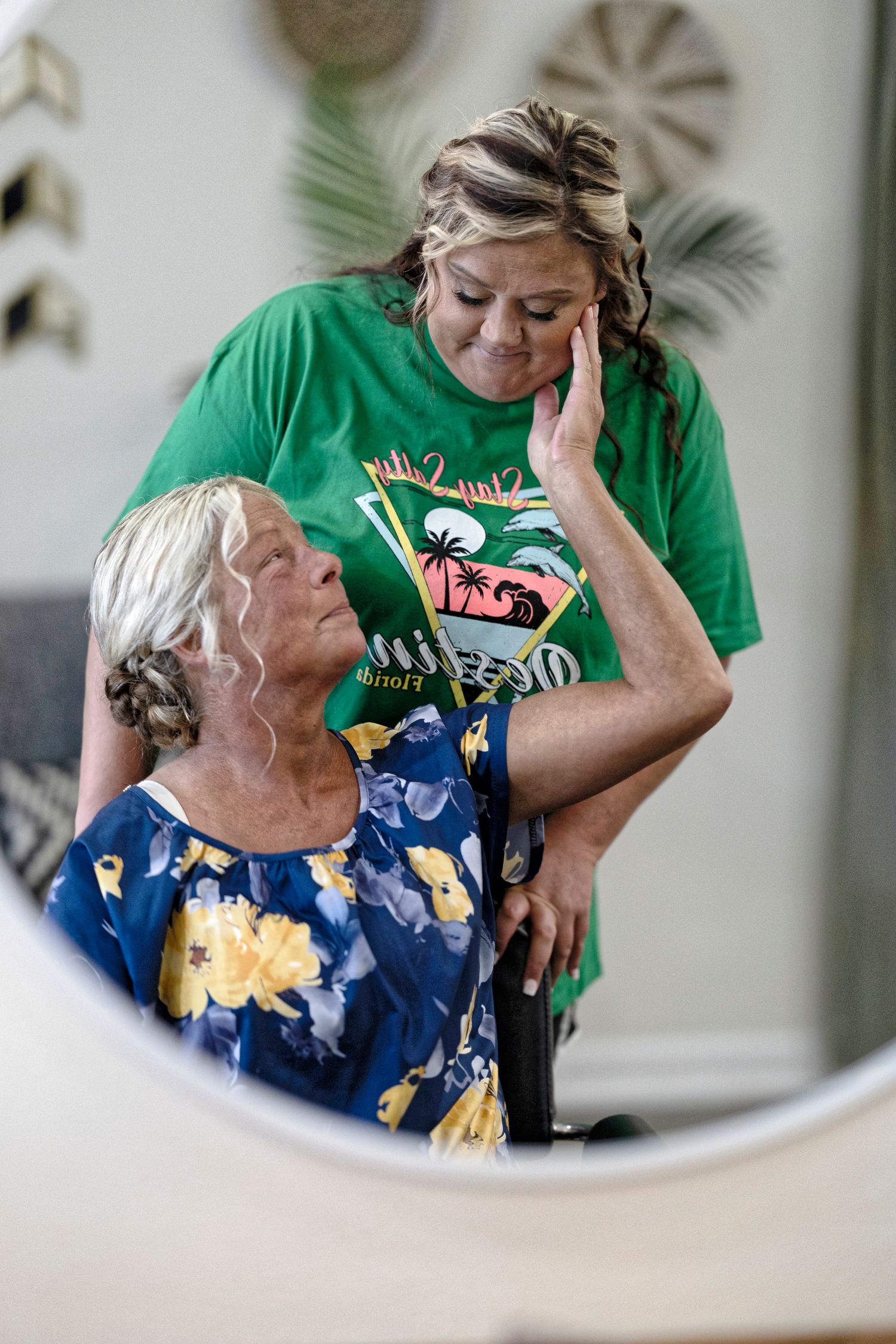 Mirror reflection shows two people in casual attire, one wearing a green t-shirt and another in a blue floral dress.