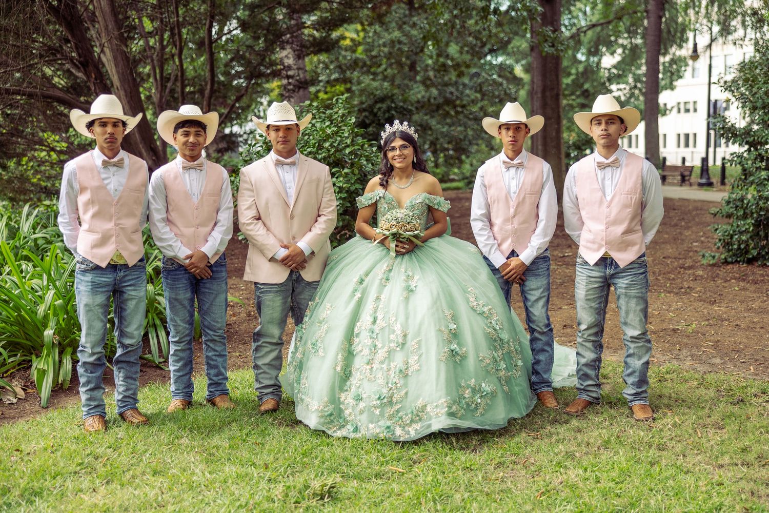 A quinceañera photo session in a park shows a group wearing cowboy attire and a mint green ball gown.