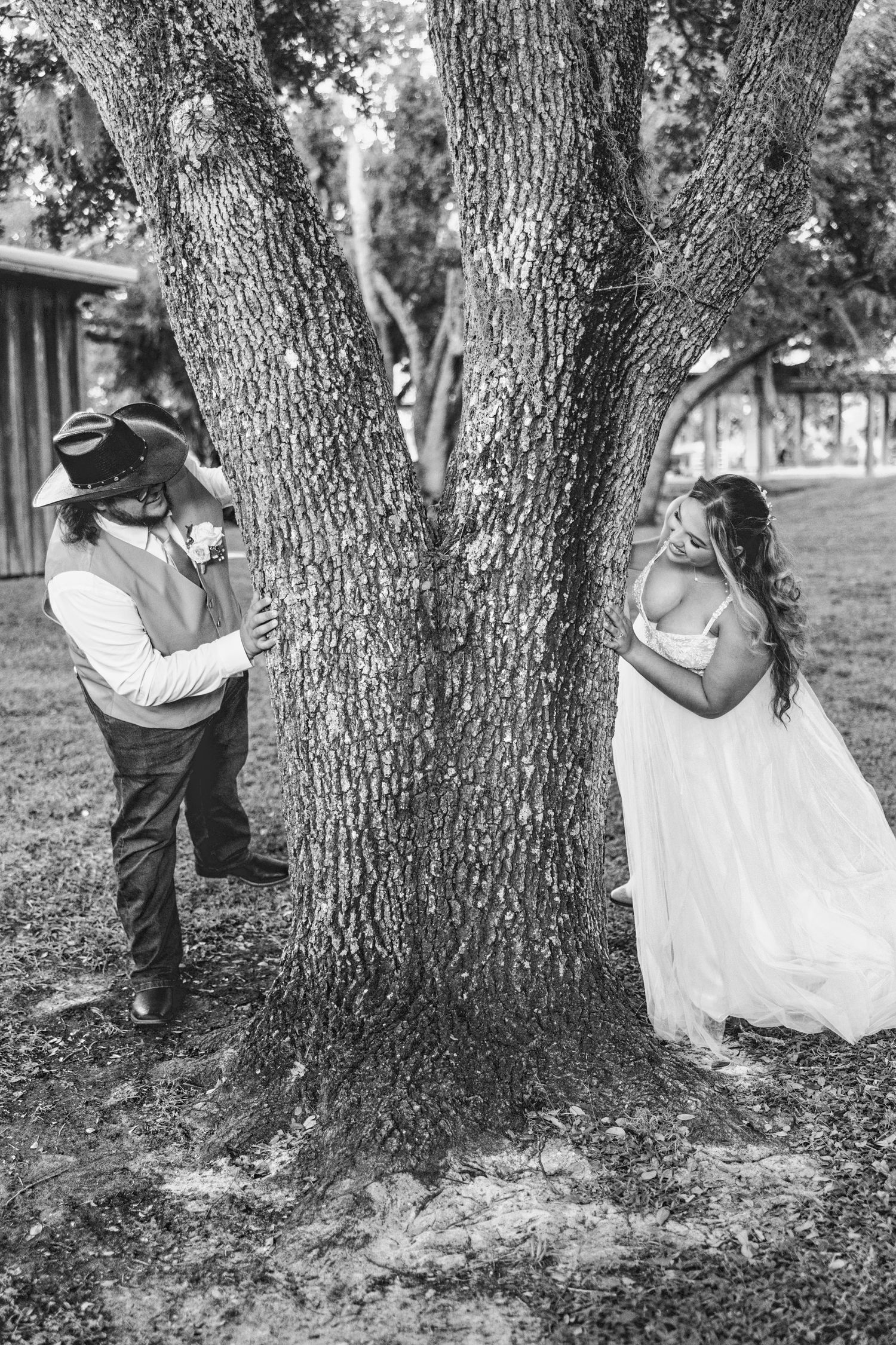 A romantic black and white photo series showing a couple sharing intimate moments behind a large tree trunk in a park setting.