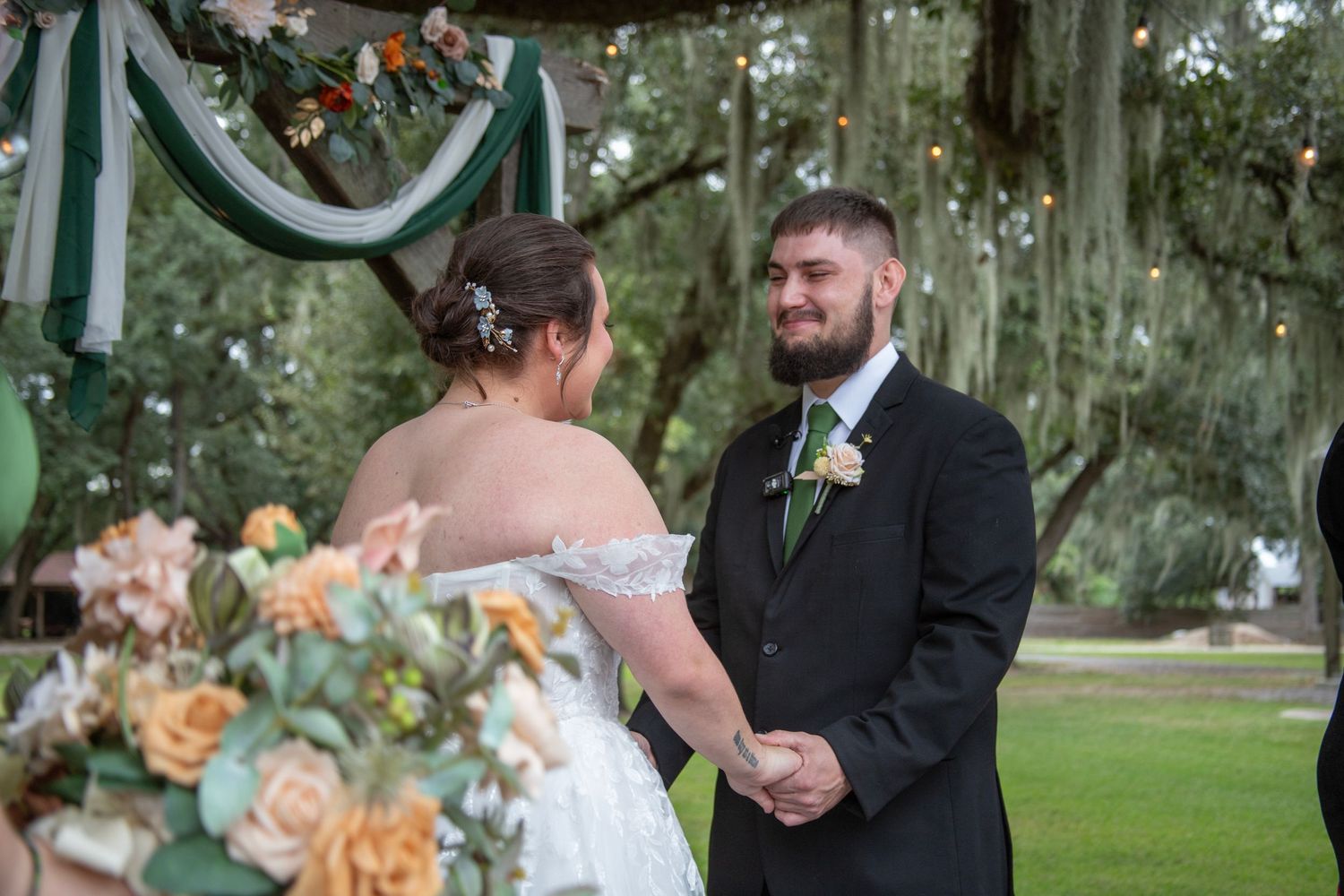 A couple shares a romantic moment in a garden setting with peach-colored floral arrangements and elegant formal attire.