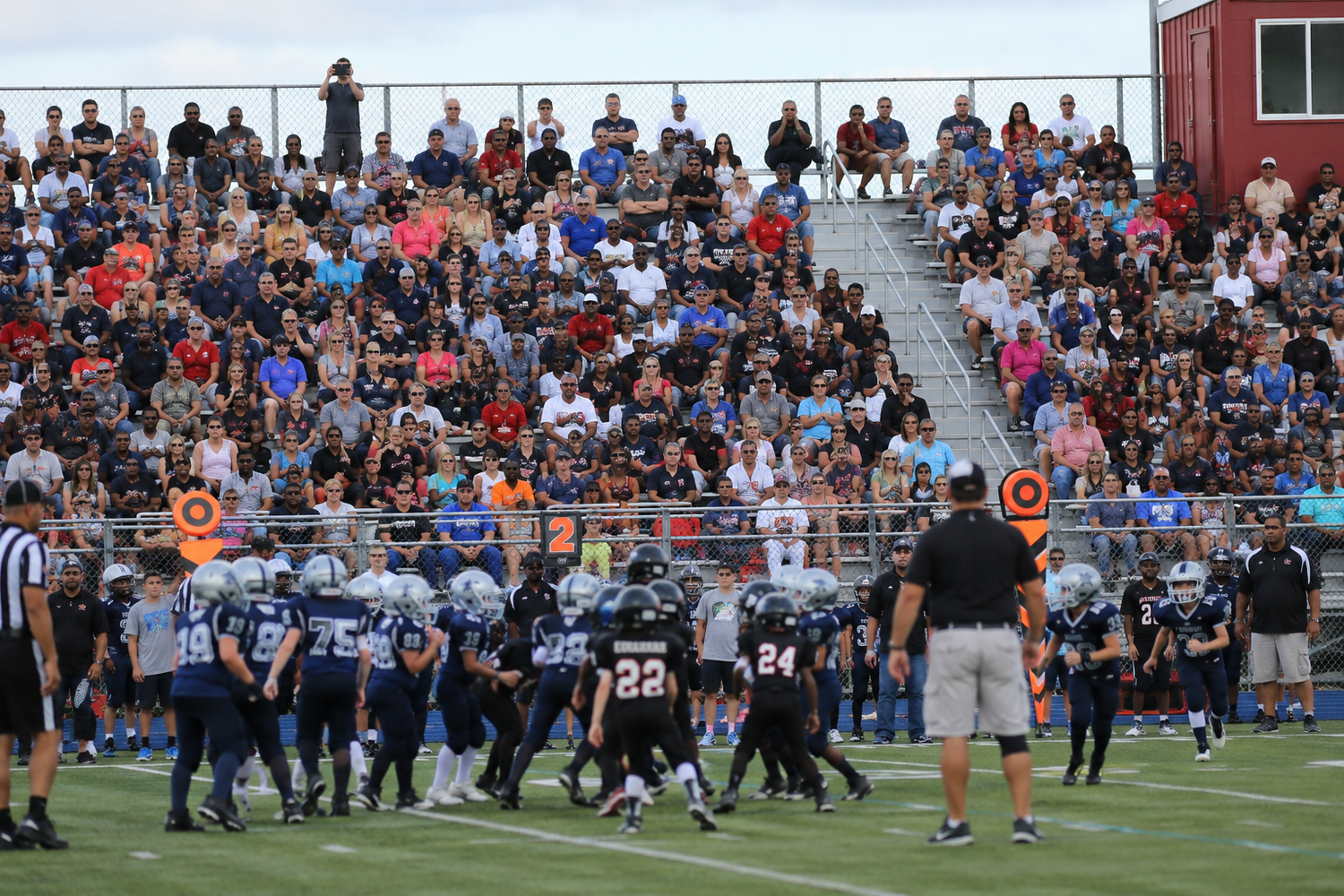 High school football teams line up on the field before a packed home stadium crowd.