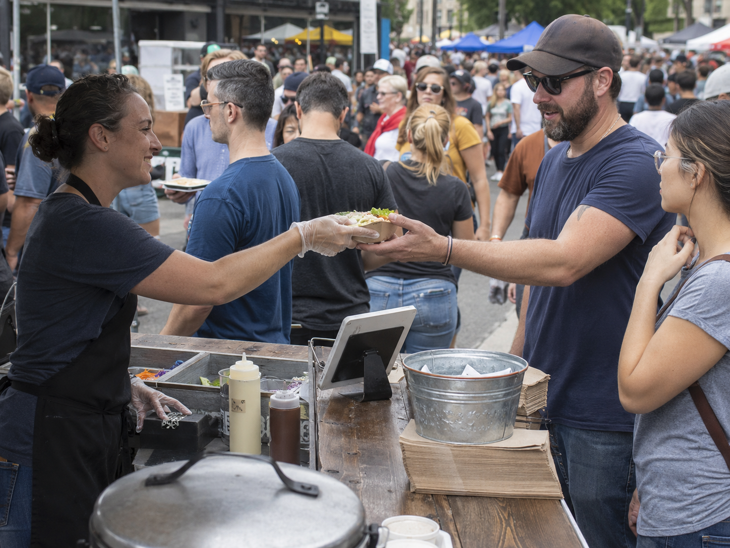 Food vendor hands meal to customer at busy outdoor street food festival market stall.