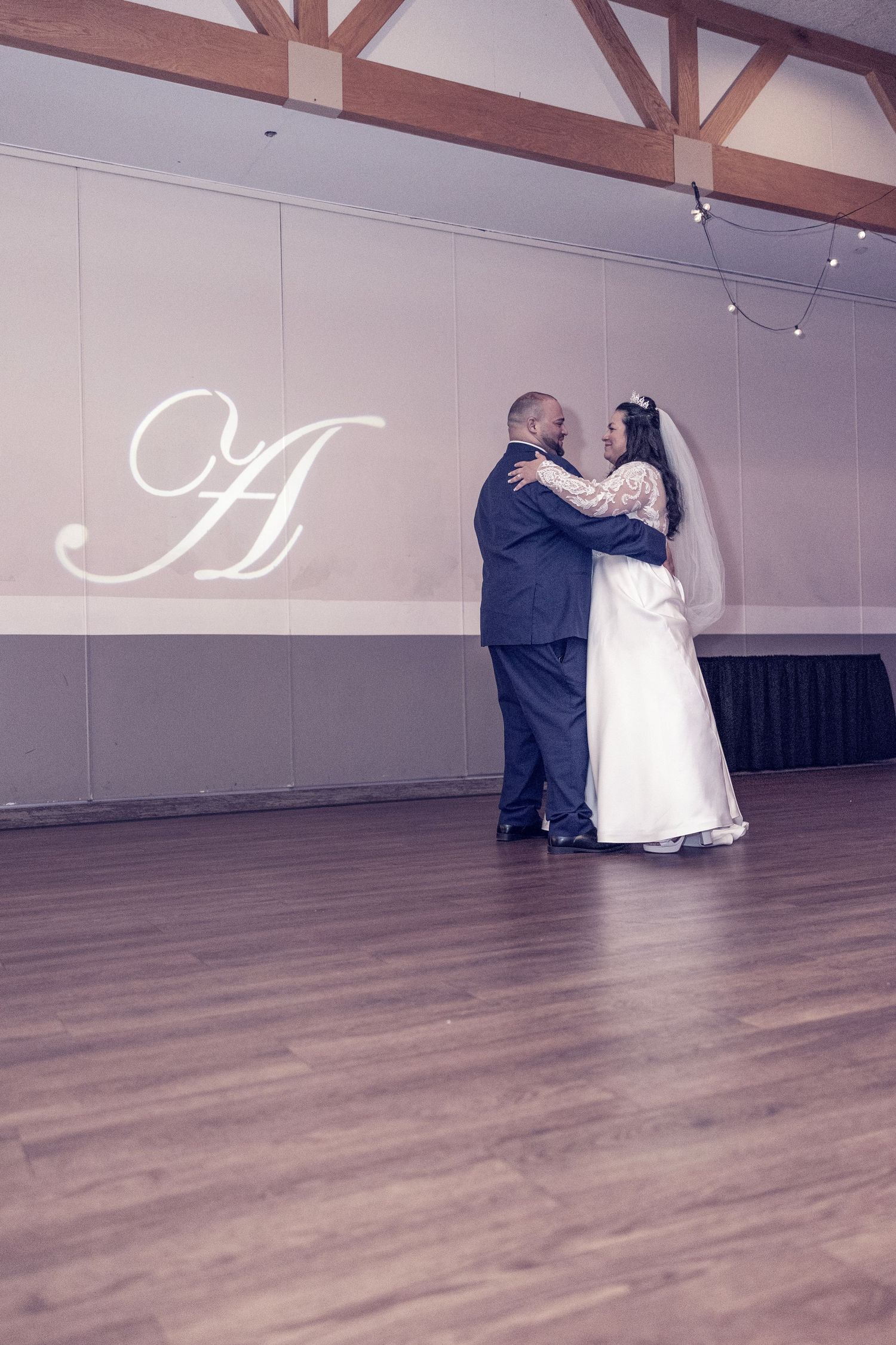 Bride and groom share their first dance in an elegant ballroom with a monogram letter A projected on the wall.