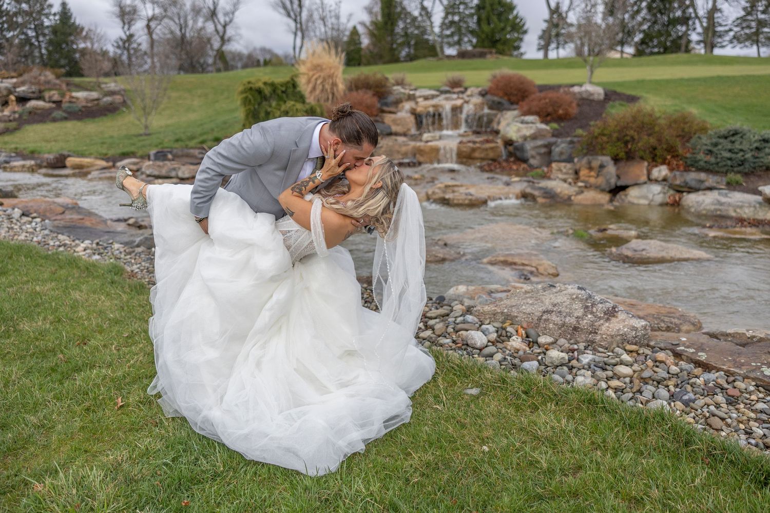 White formal dress flowing in the breeze beside a decorative rock garden with waterfall feature.
