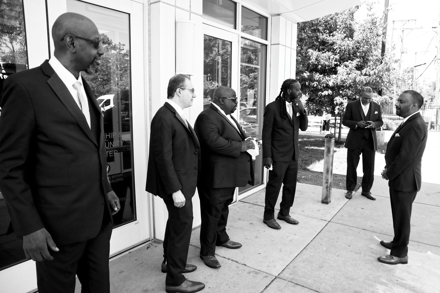 Black and white photo of a group of men in suits socializing outside a building entrance at a formal event.
