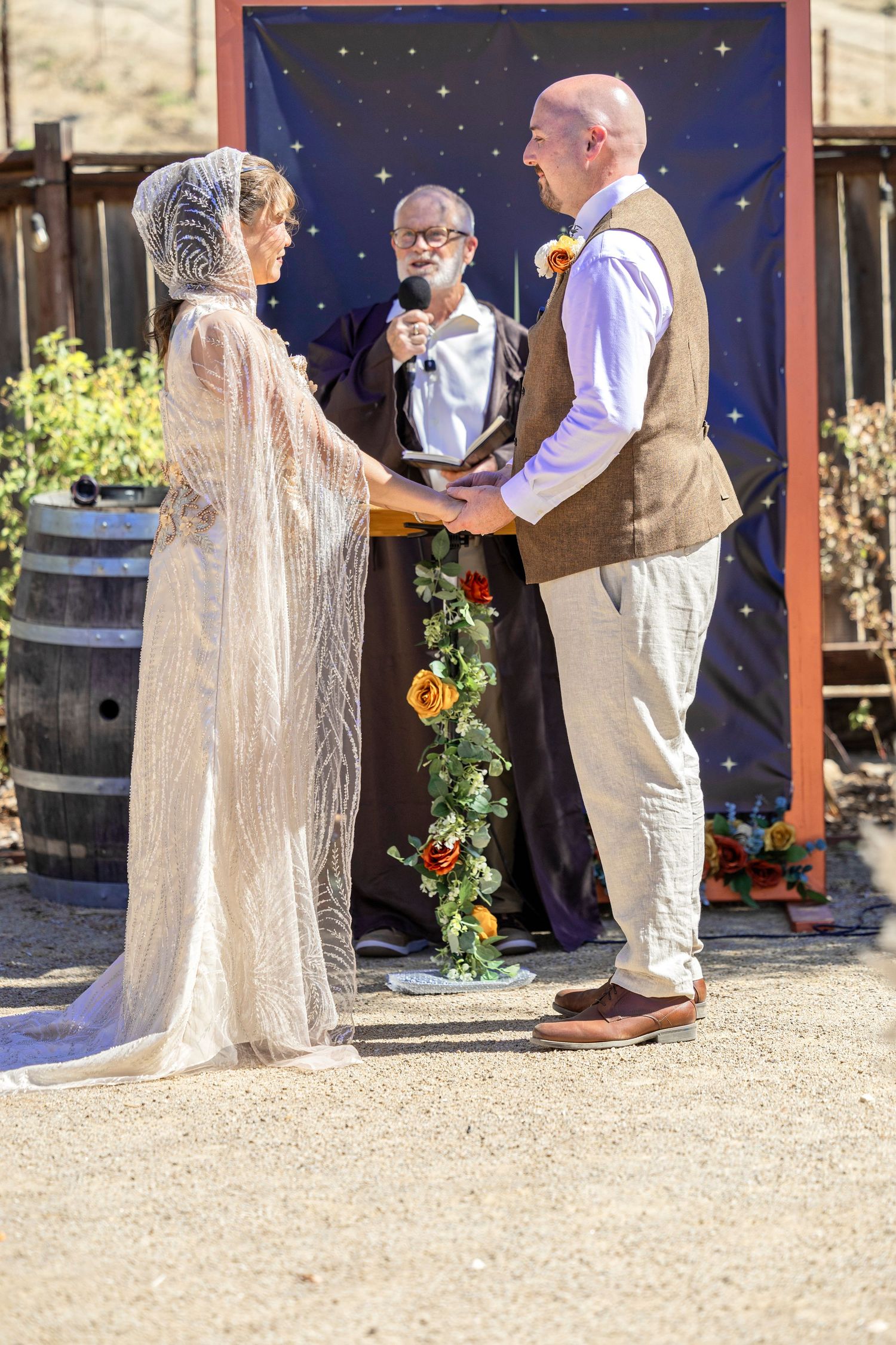 Bride and groom exchange vows outdoors at rustic wedding ceremony with officiant and starry backdrop.