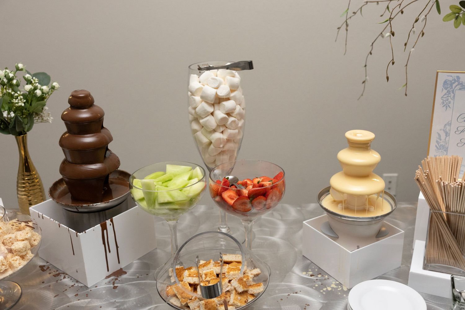 Elegant dessert table with chocolate fountains, marshmallows, strawberries, and honeydew melon dipping treats.