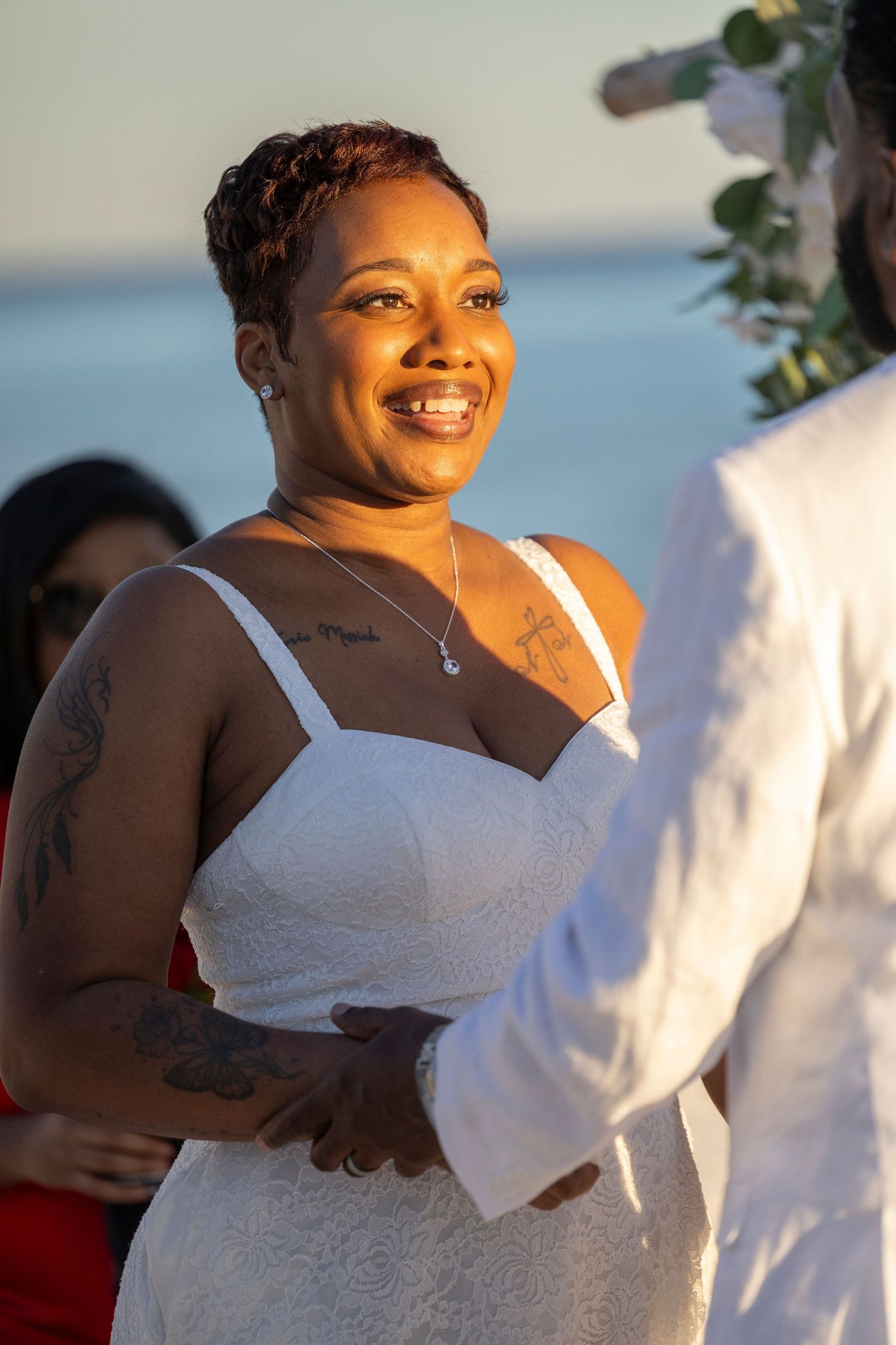 A person wearing a white wedding dress smiles joyfully during a sunny outdoor celebration.