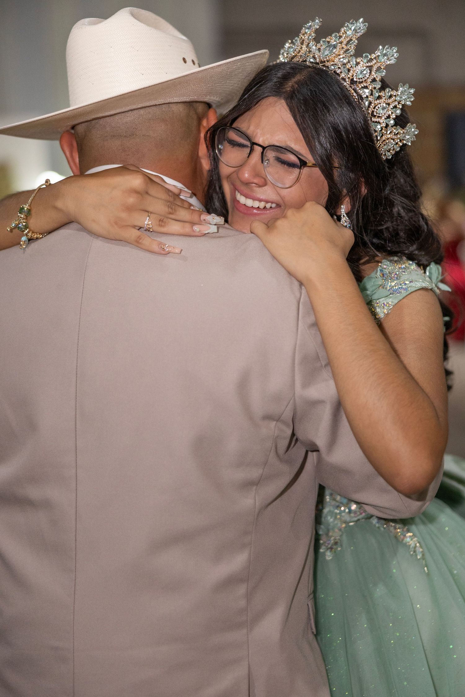 A couple embraces during a dance, with the person in a mint green gown wearing a sparkling crown.