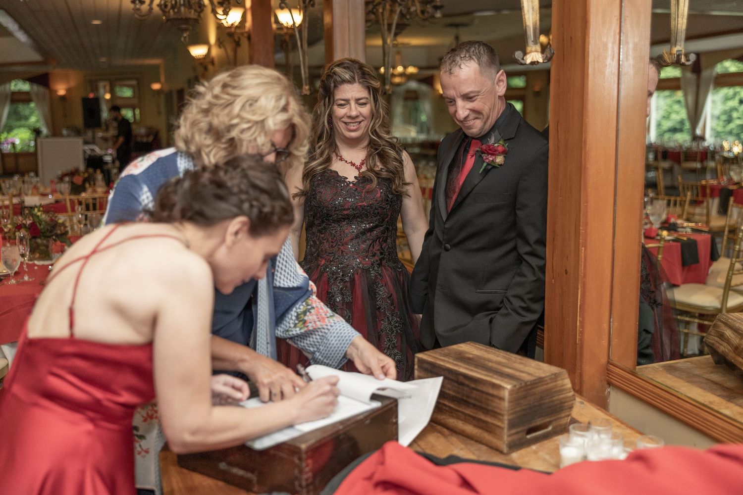 Wedding guests sign the guestbook at an elegant indoor reception venue while others look on with smiles.