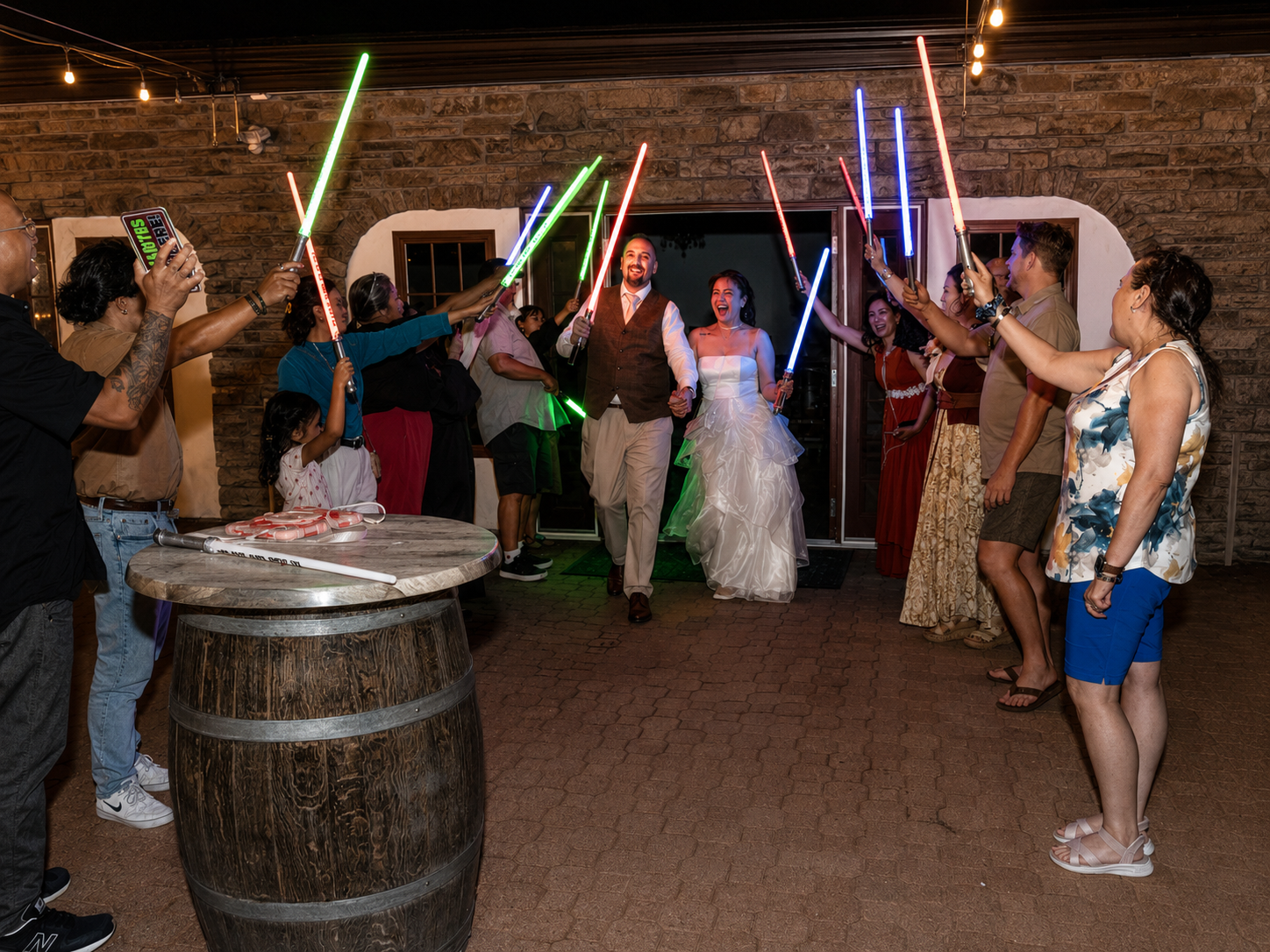 Star Wars themed wedding exit with guests holding colorful lightsabers as bride and groom walk through.