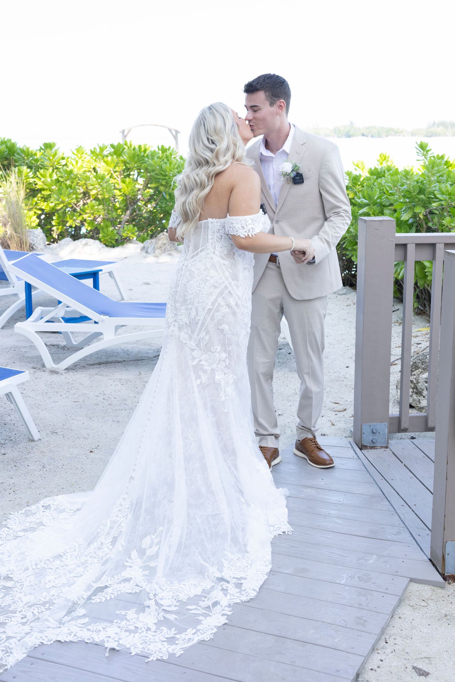 A romantic wedding couple shares a dip kiss on a beachfront deck during sunset.