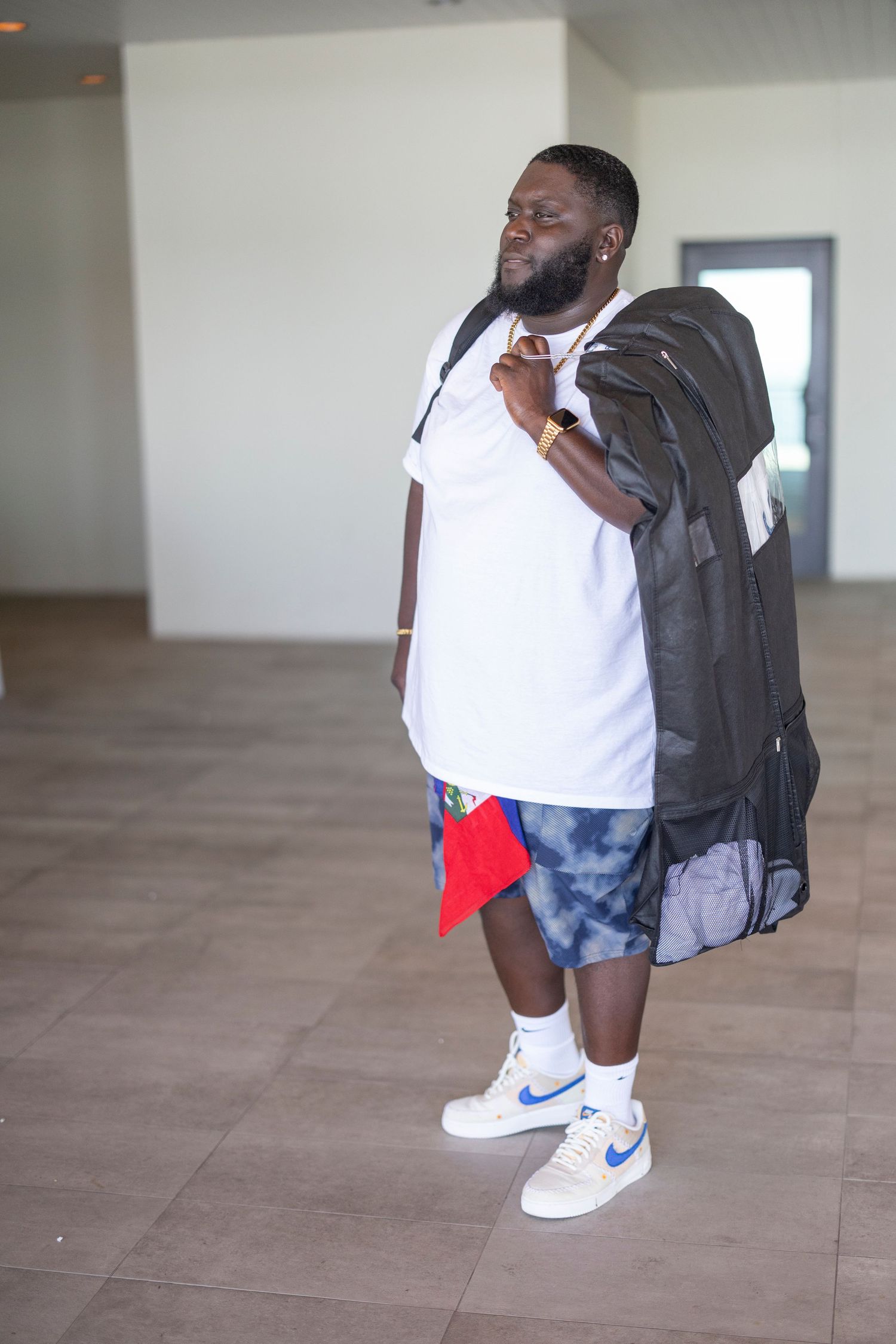 A person in a white t-shirt and blue shorts crouches down to show off their Nike sneakers on a tiled floor.
