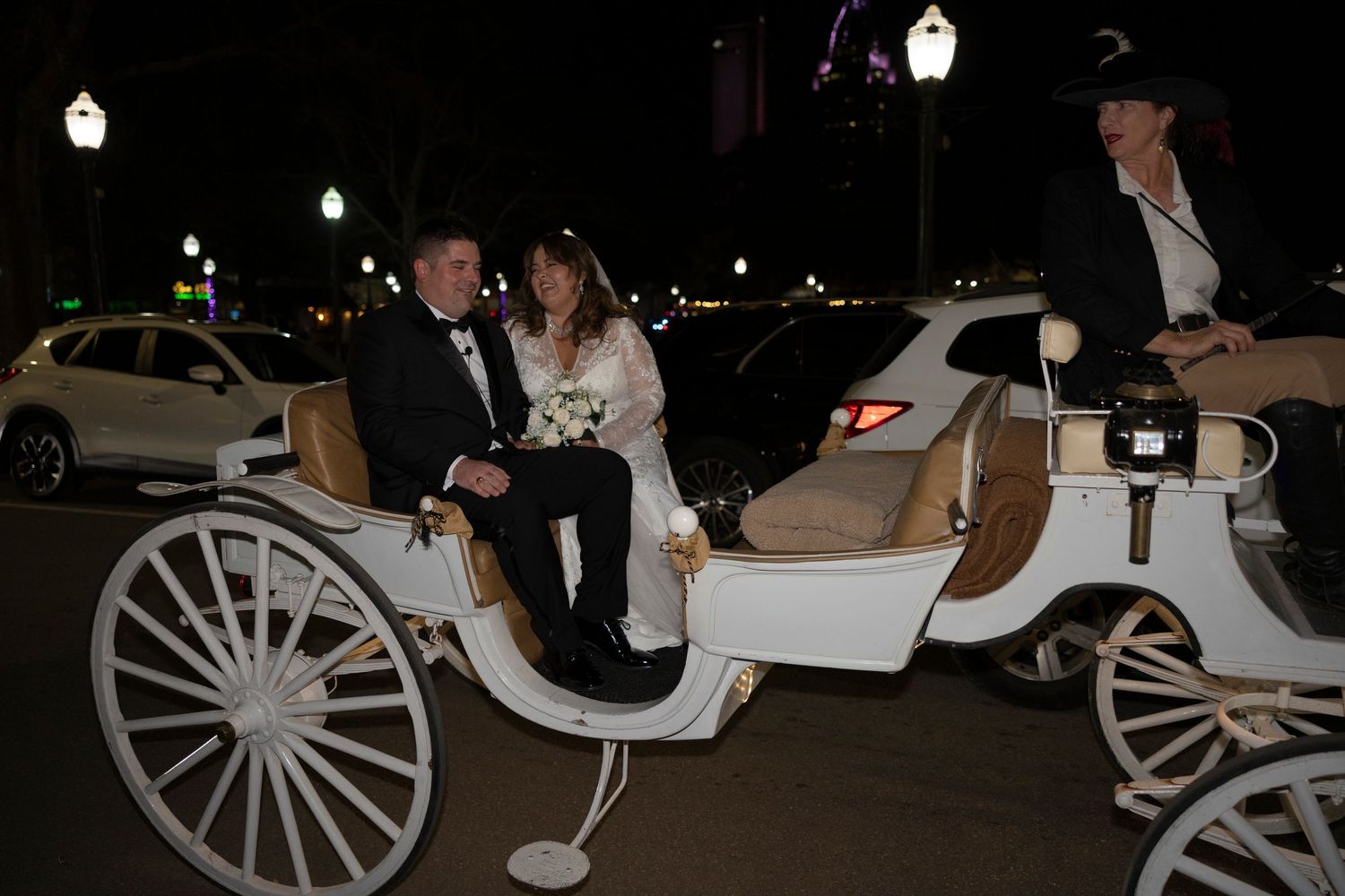 A white horse-drawn carriage with passengers illuminated at night on a city street.