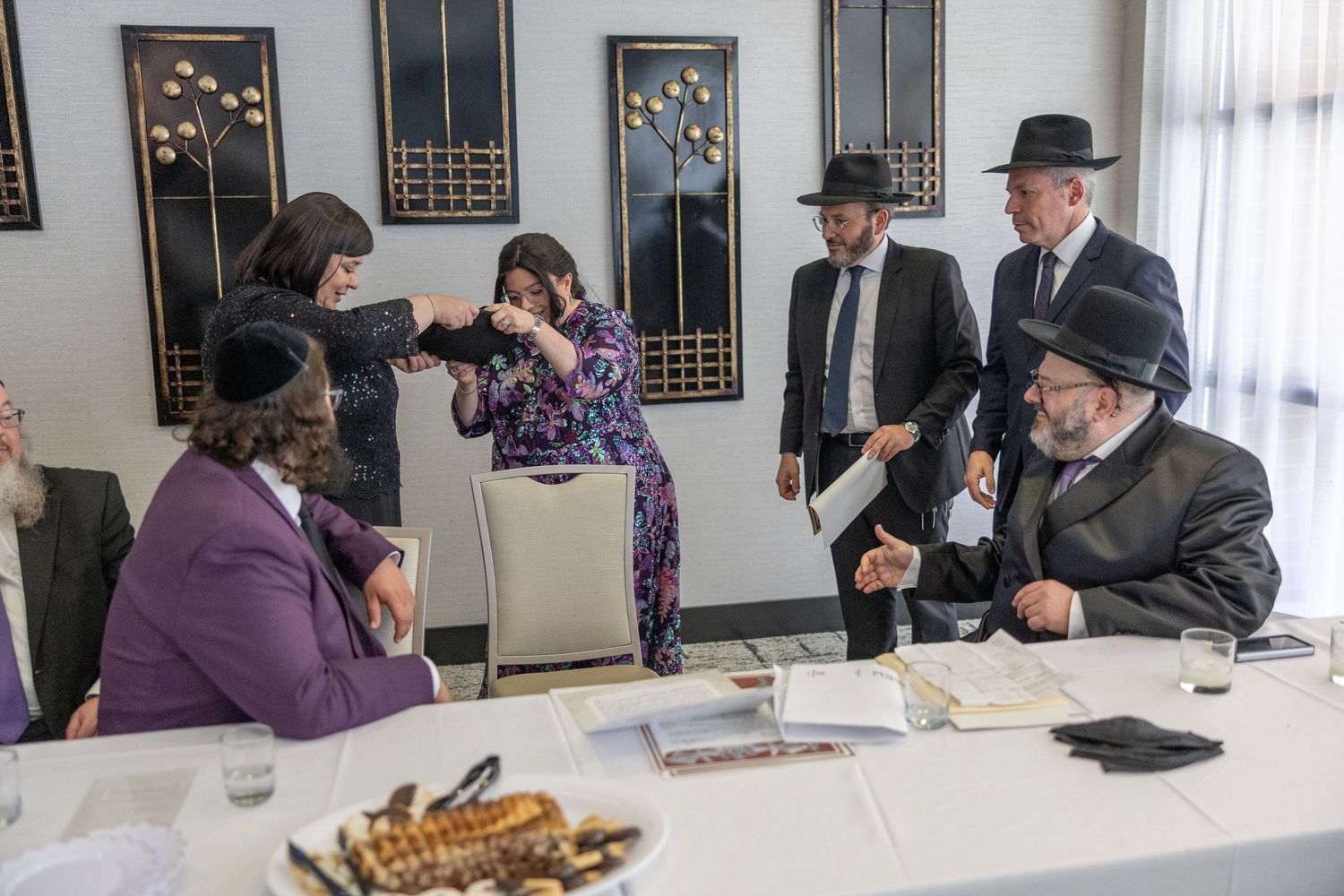 People gather at a long table for a traditional Jewish meal with challah bread and religious observances.