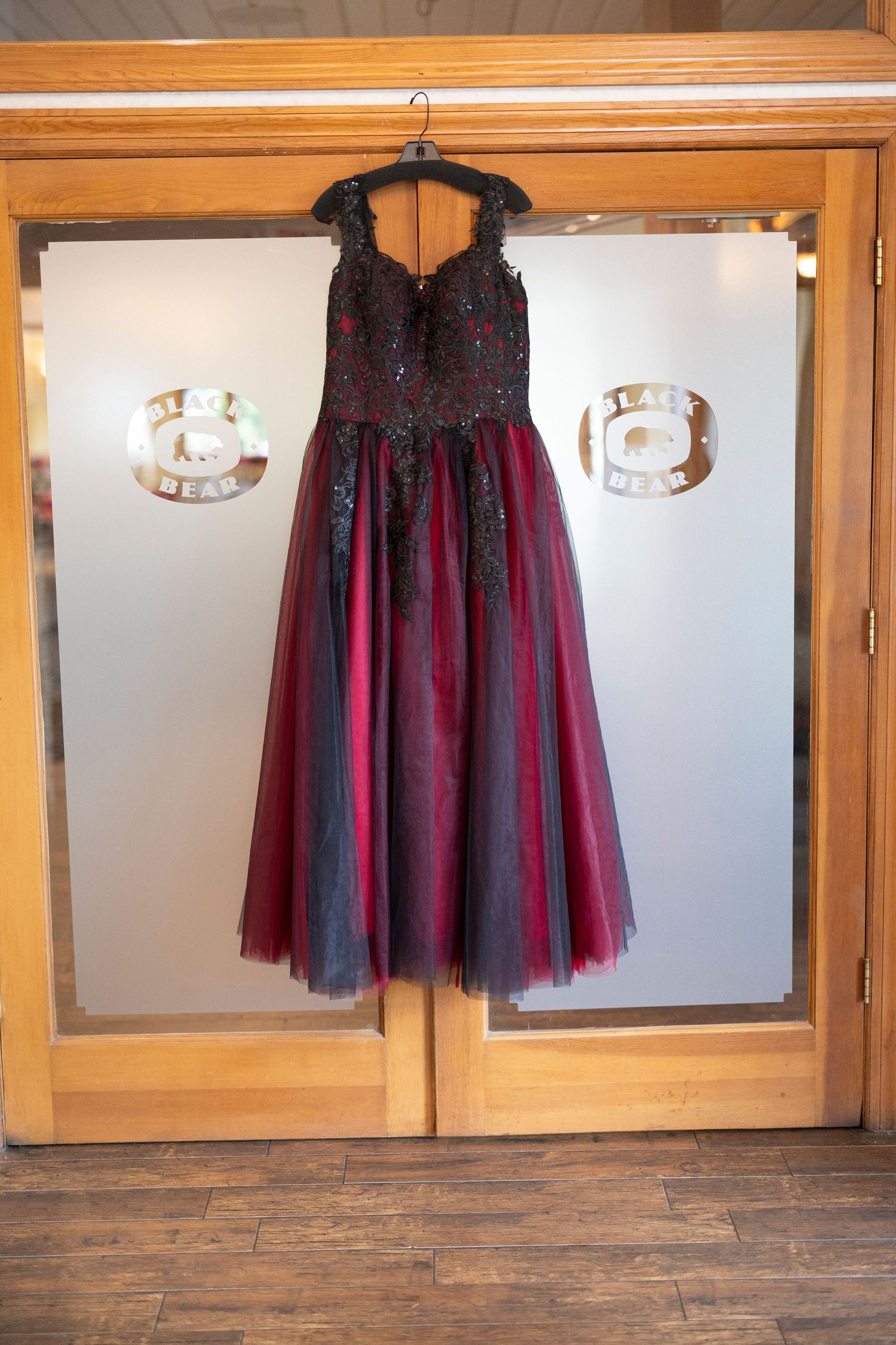 A black and burgundy tulle tutu skirt displayed on a hanger against wooden cabinets with glass panels.