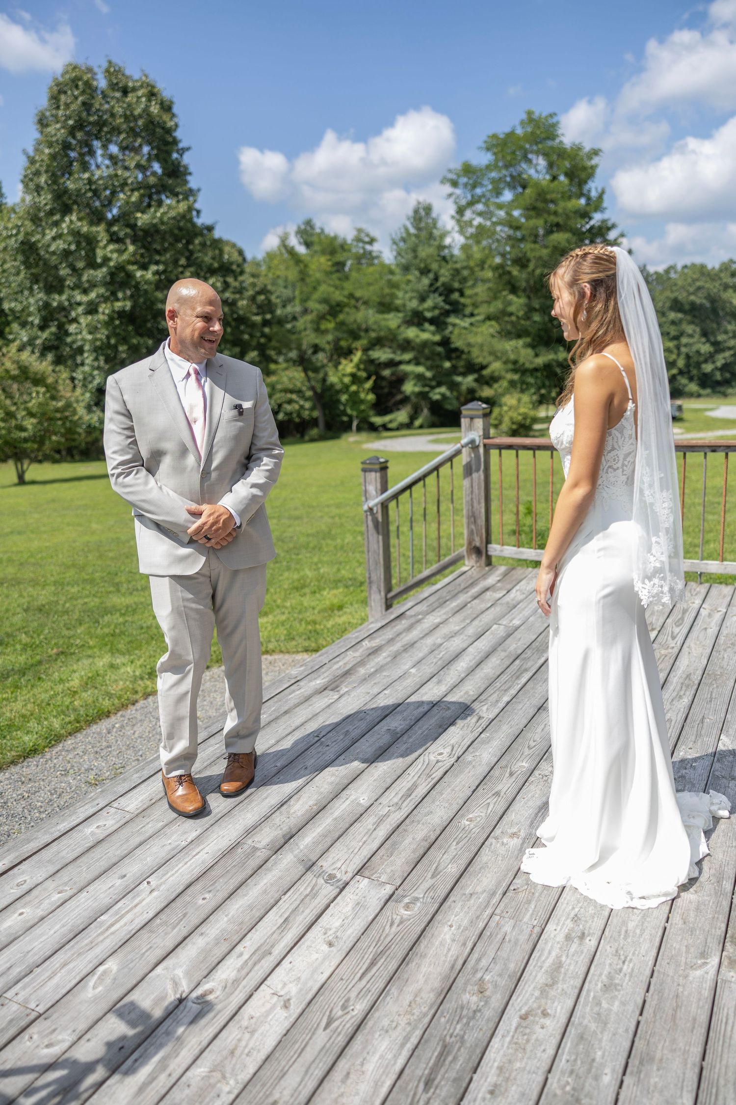A couple shares a special moment on a wooden deck surrounded by lush green trees on a sunny summer day.