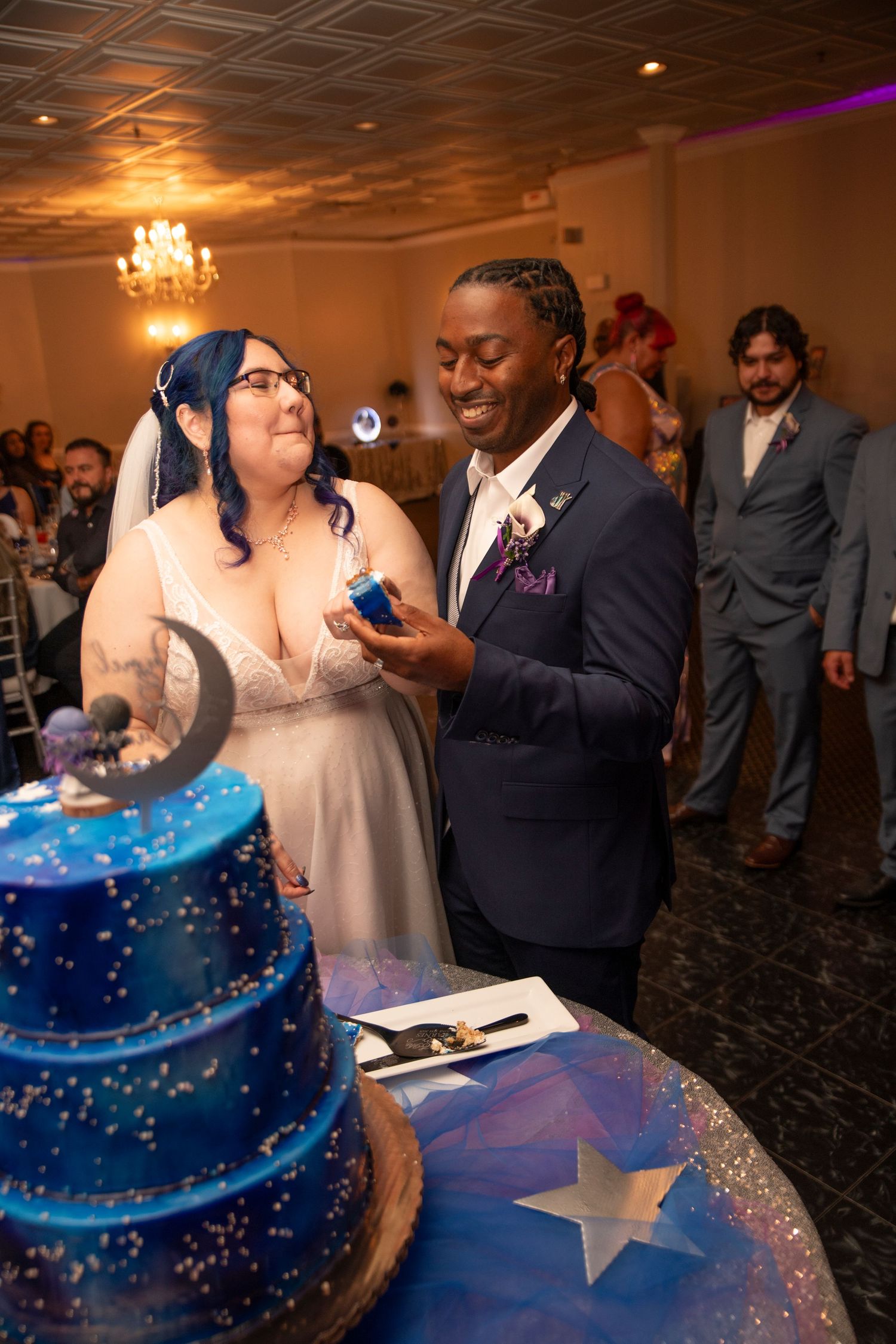 Wedding couple cuts into a stunning blue and white tiered cake decorated with stars at their reception celebration.