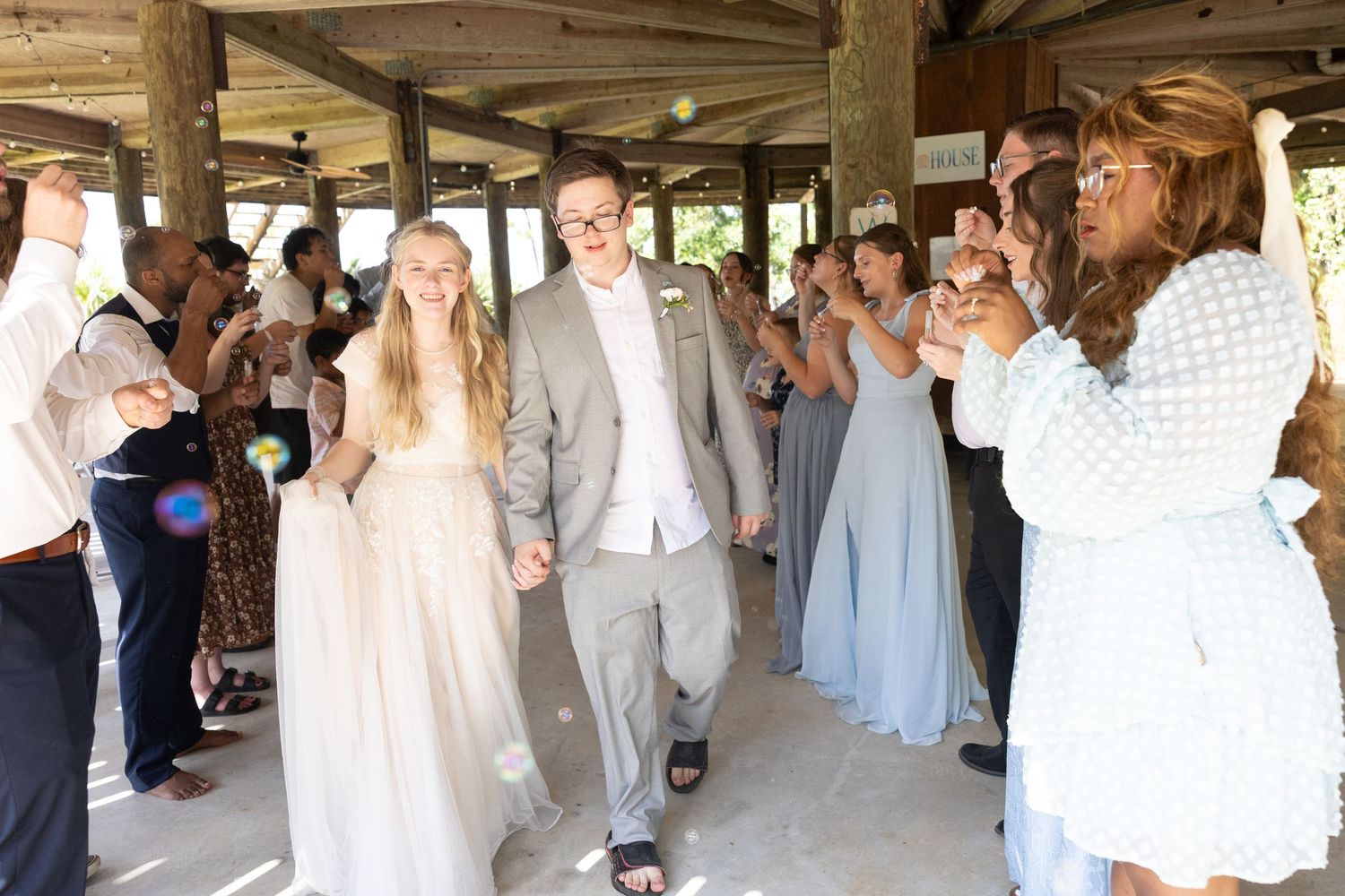 A panoramic view of wedding guests gathered under a rustic wooden pavilion during a celebration ceremony.
