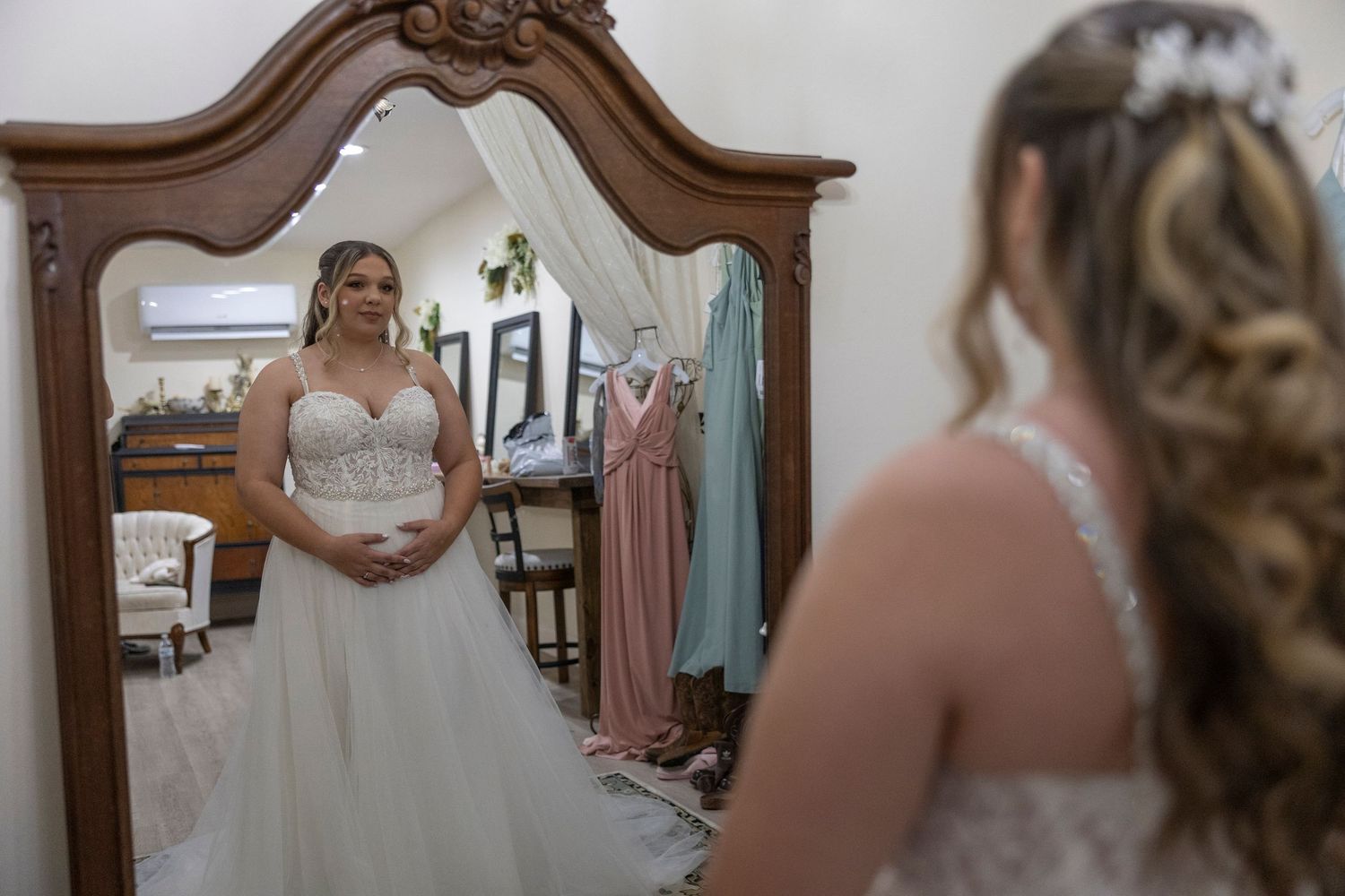 A group of people in a bridal boutique trying on pink bridesmaid dresses and wedding gowns.