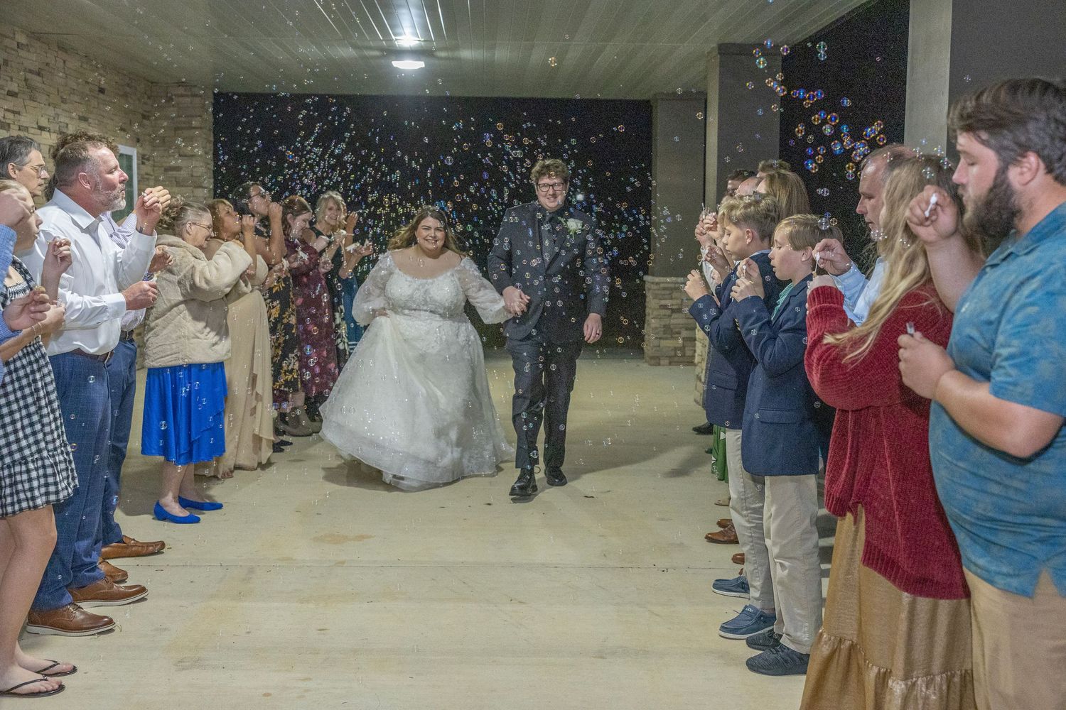 Wedding guests line a hallway throwing confetti as newlyweds walk through during their reception celebration.