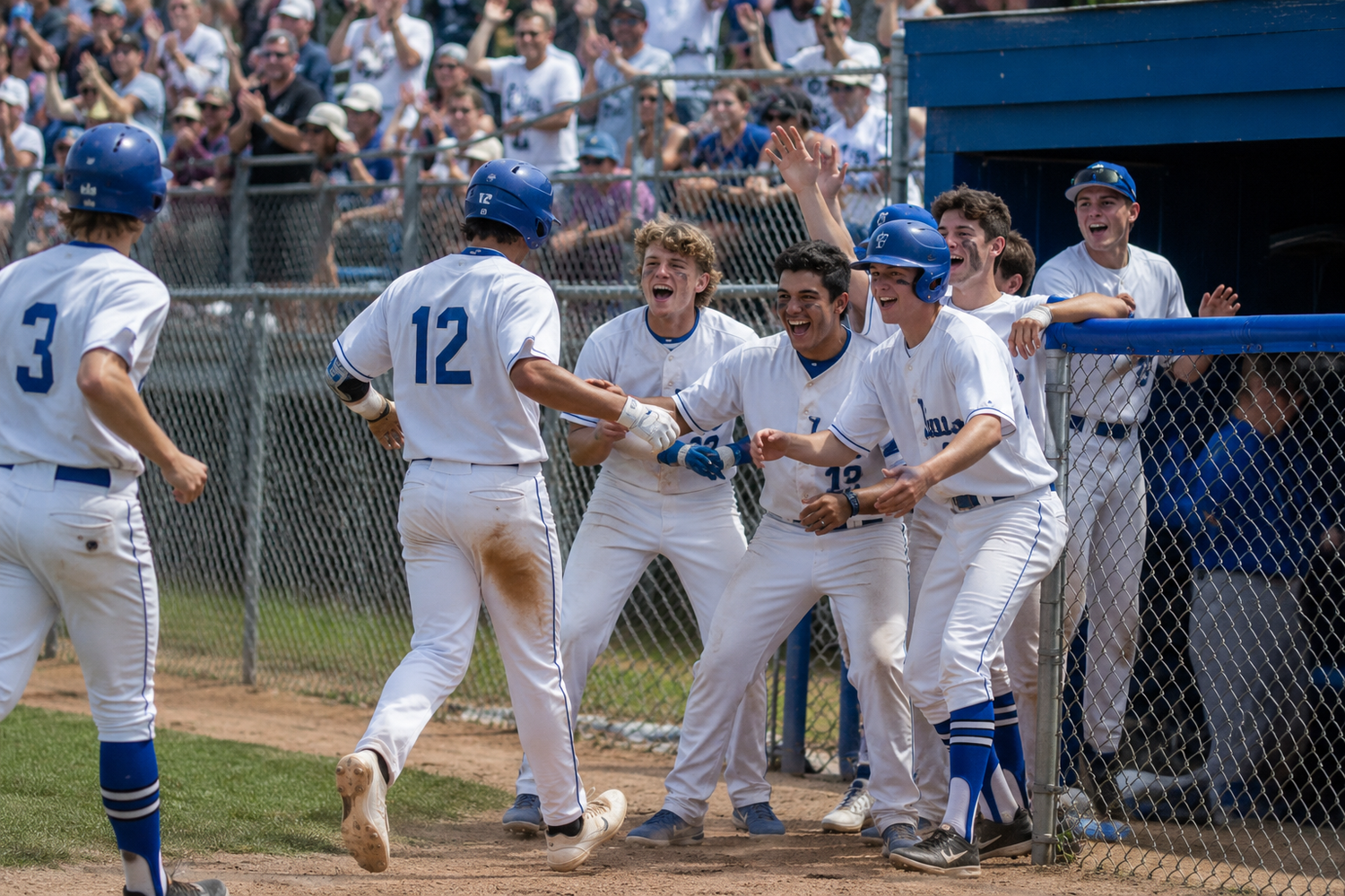 Baseball team in blue uniforms celebrates enthusiastically near dugout fence after a scoring play during game.