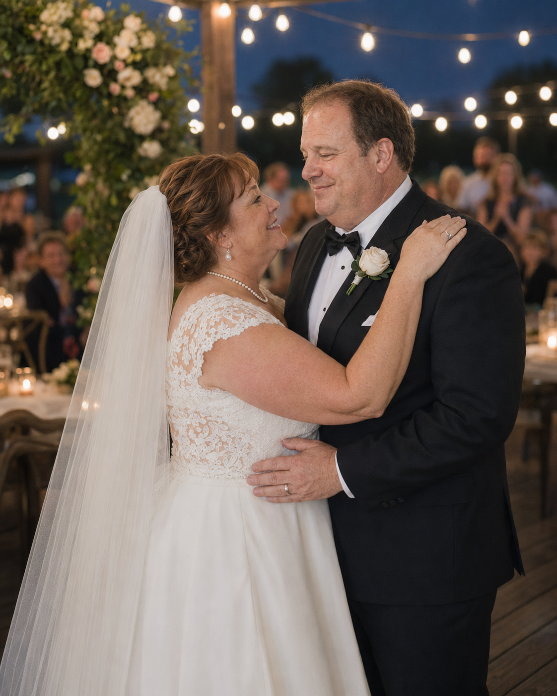 Bride and groom share their first dance under romantic string lights at an elegant outdoor evening wedding reception.