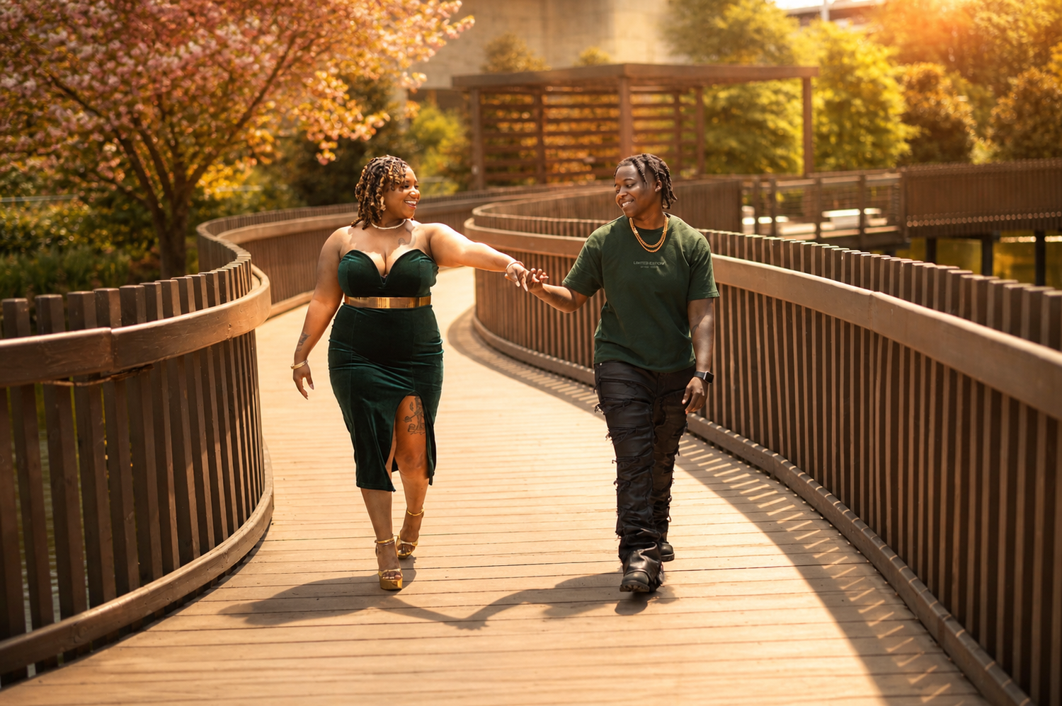 Couple holding hands walking on a wooden bridge surrounded by autumn trees in golden hour light.