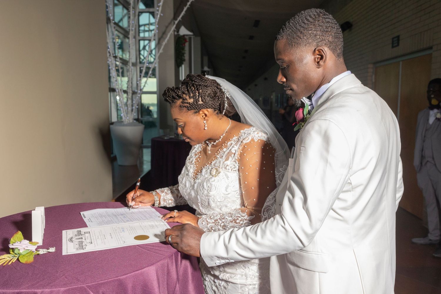 Bride and groom signing wedding certificate at purple draped table during elegant indoor wedding ceremony.