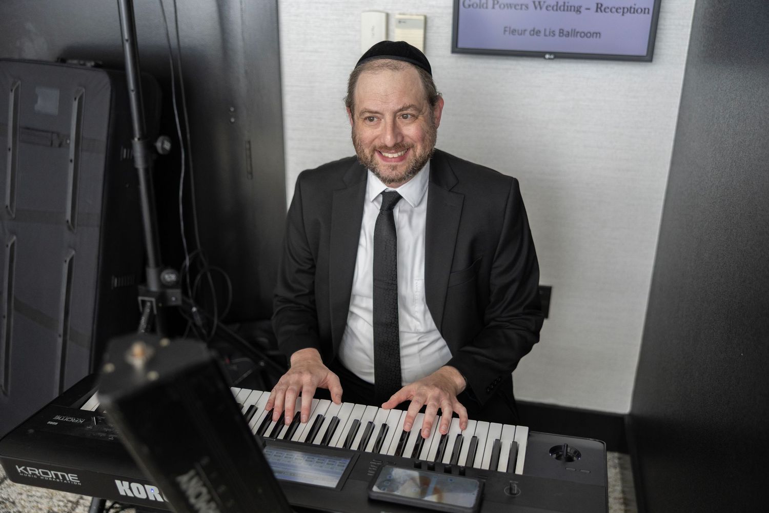 Professional musician in a dark suit plays a keyboard synthesizer at an event venue.