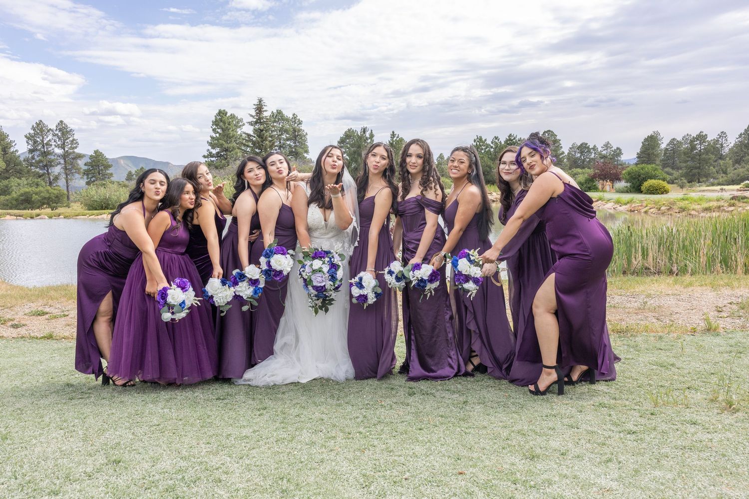 Wedding party in purple bridesmaid dresses poses outdoors for group photos on a sunny day.