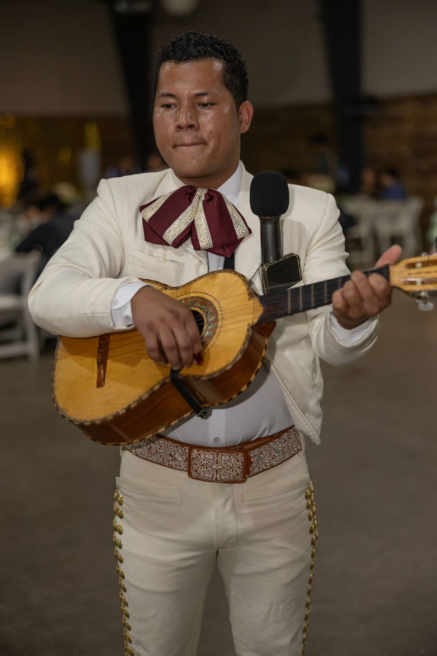 A mariachi musician in traditional white charro suit plays a guitarron during a performance.