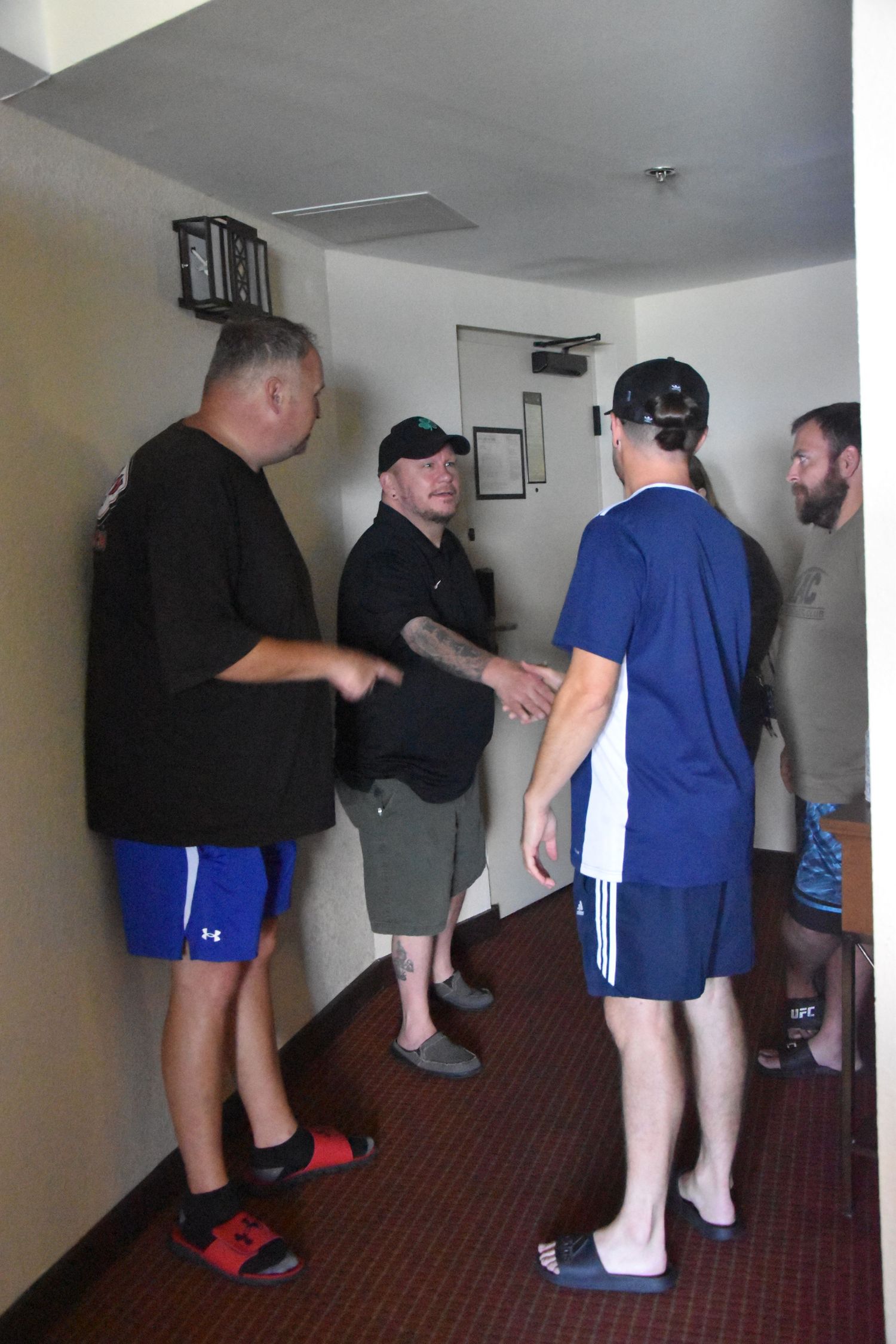 Three people in athletic wear stand in a hallway having a conversation.