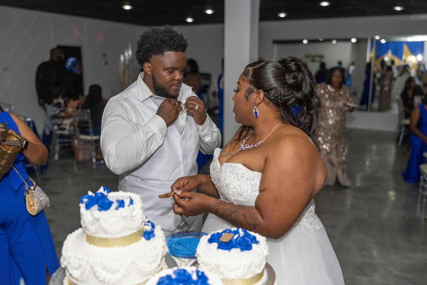 Bride and groom cutting their white and blue wedding cake at a elegant indoor wedding reception celebration.