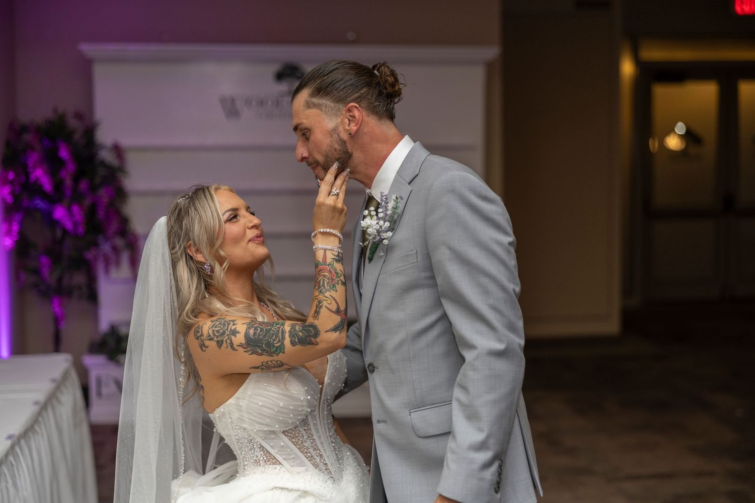 A tender moment between newlyweds sharing an intimate interaction at their wedding reception with purple lighting.