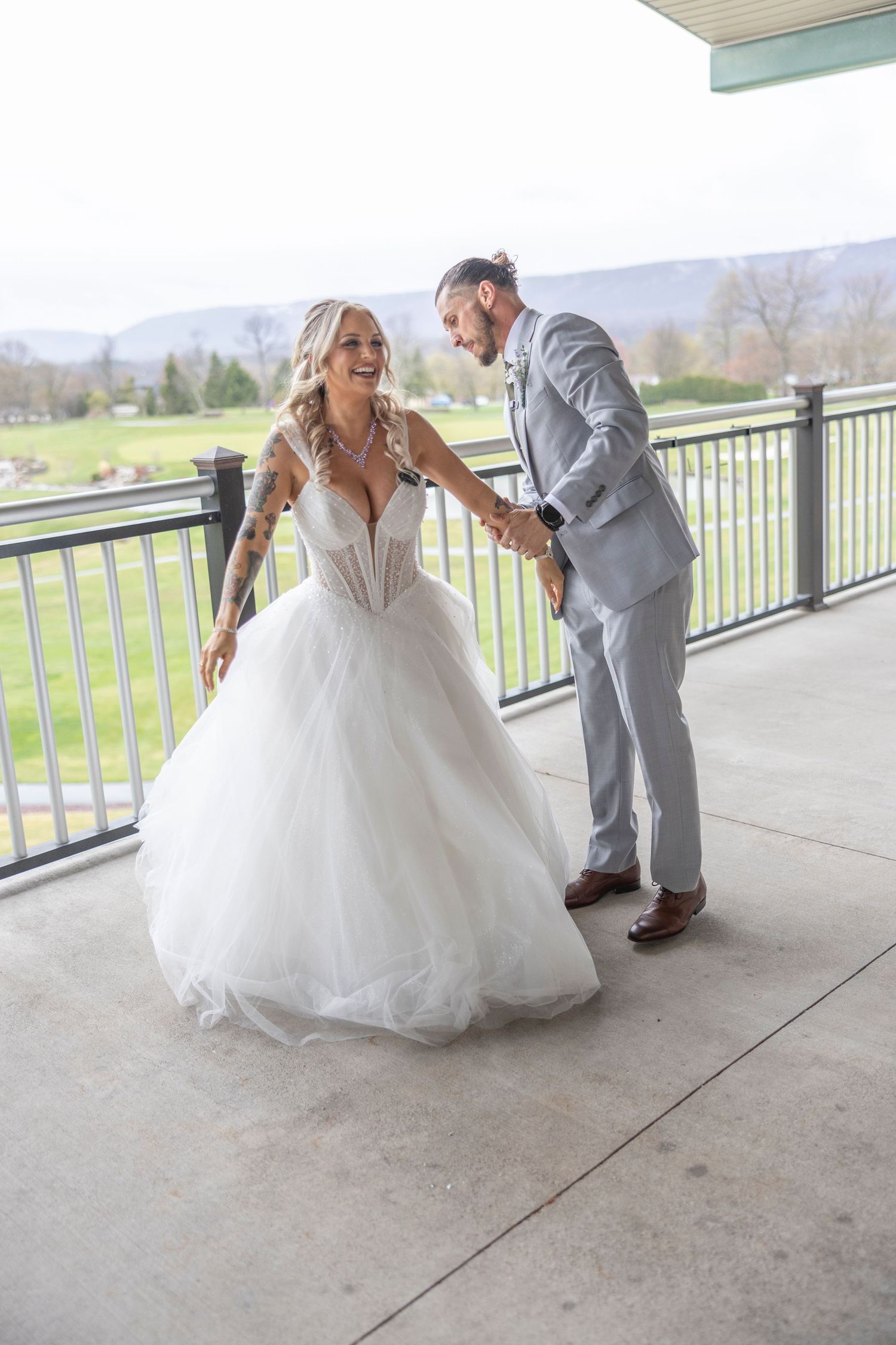 A wedding couple shares a joyful moment together on a covered patio overlooking a peaceful countryside landscape.