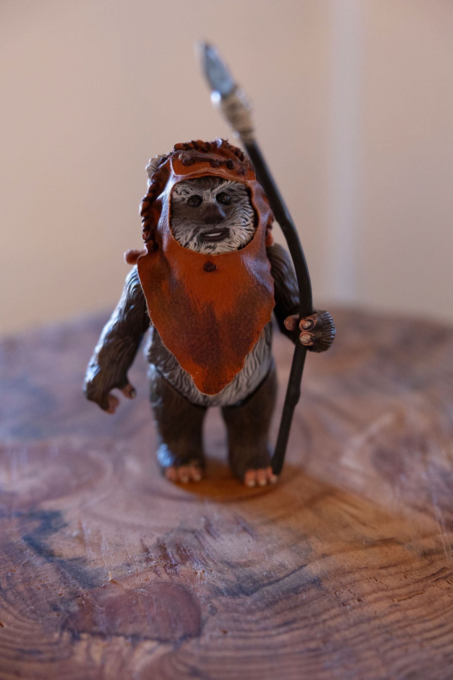 Star Wars Ewok action figure holding a spear, standing on a wooden surface, wearing an orange hood.