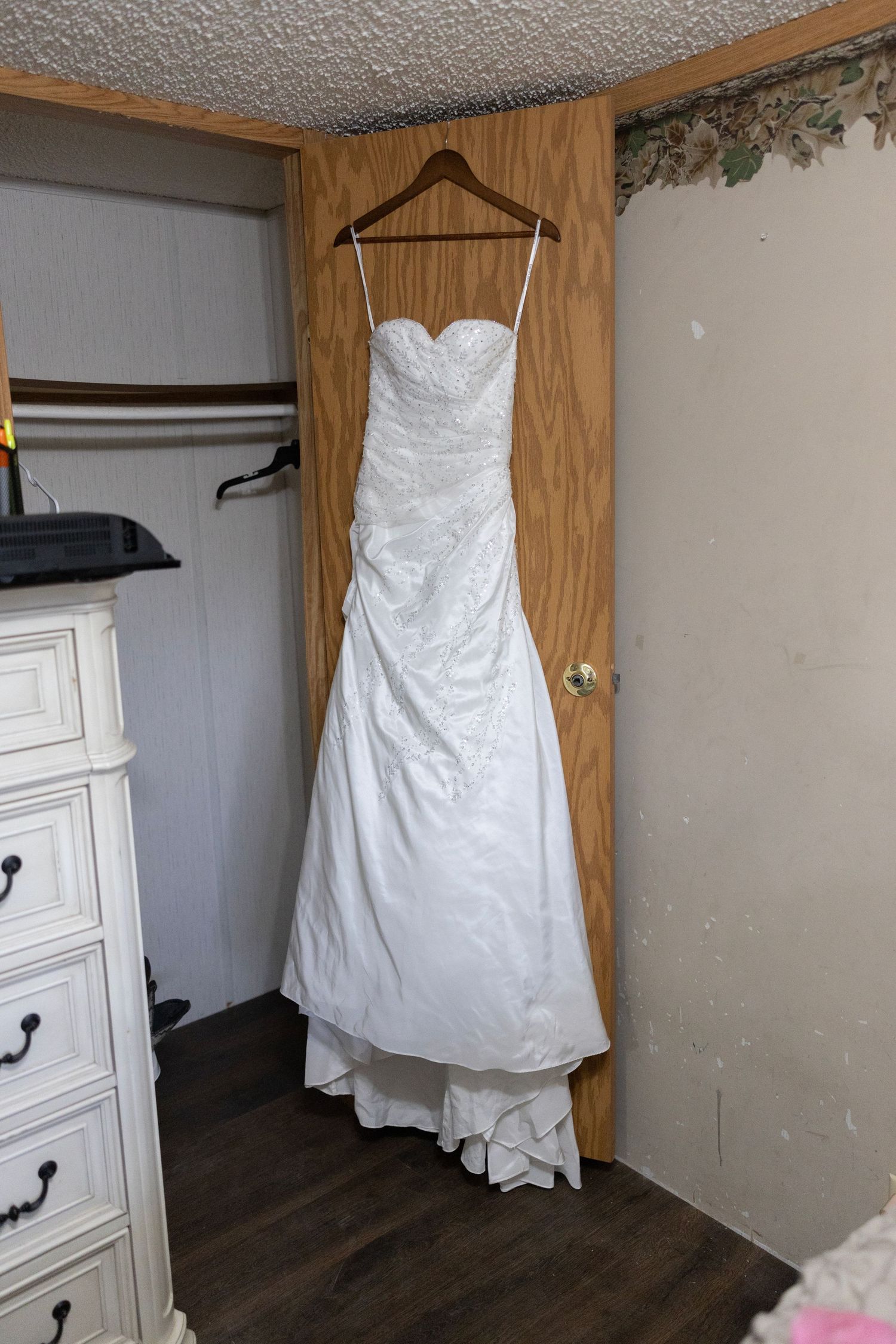 White strapless sweetheart neckline wedding gown hanging on wooden door in bedroom.
